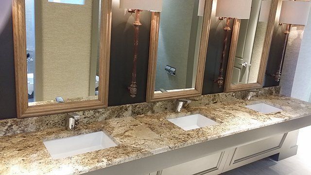 Three sinks with mirrors, cream cabinets, and granite countertop in a restroom.