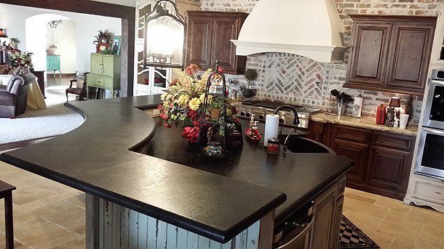 Kitchen with dark countertop island and brick backsplash. Wooden cabinets, appliances.