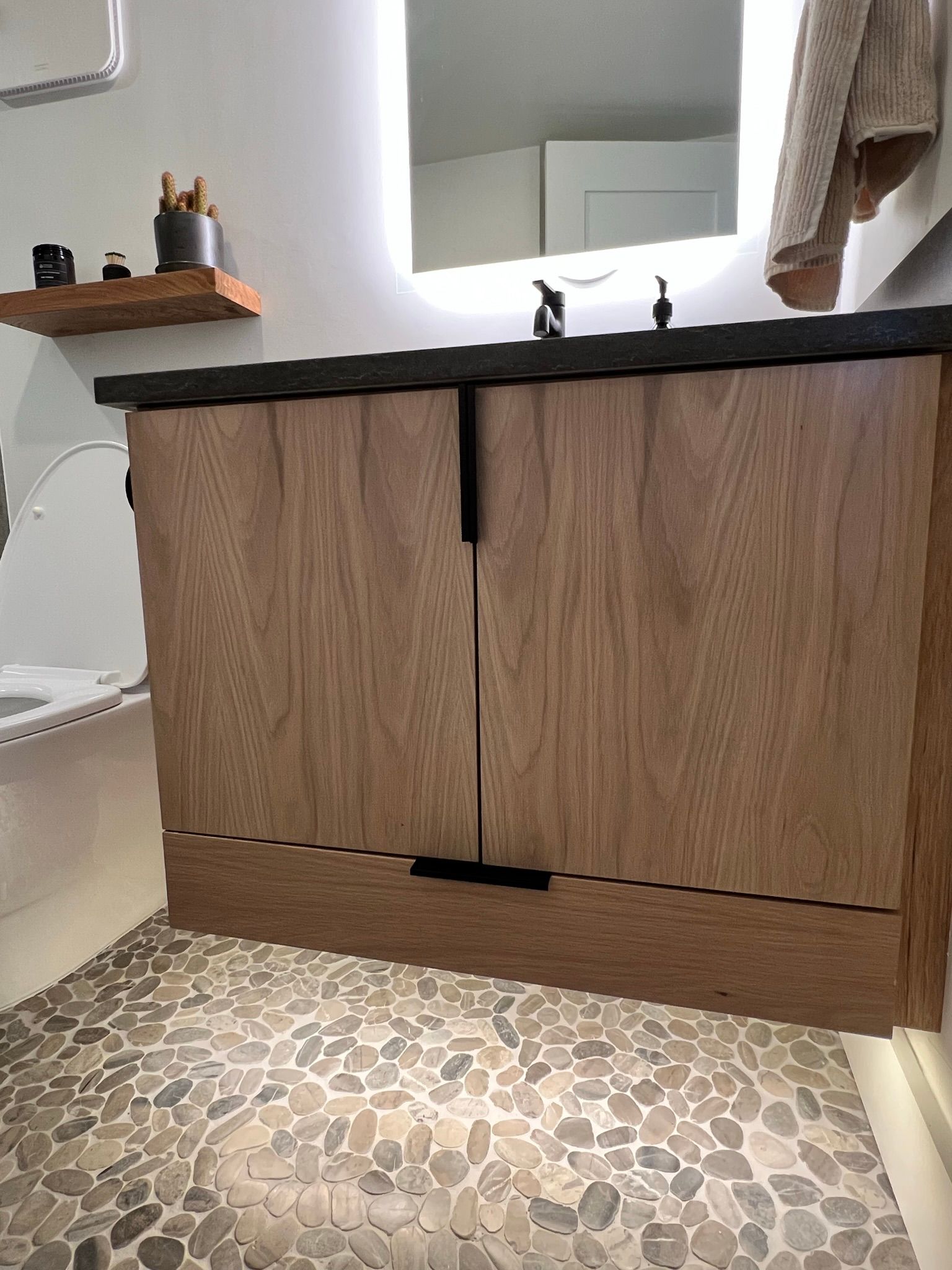 Bathroom vanity with wooden doors, dark countertop, and pebble tile floor.
