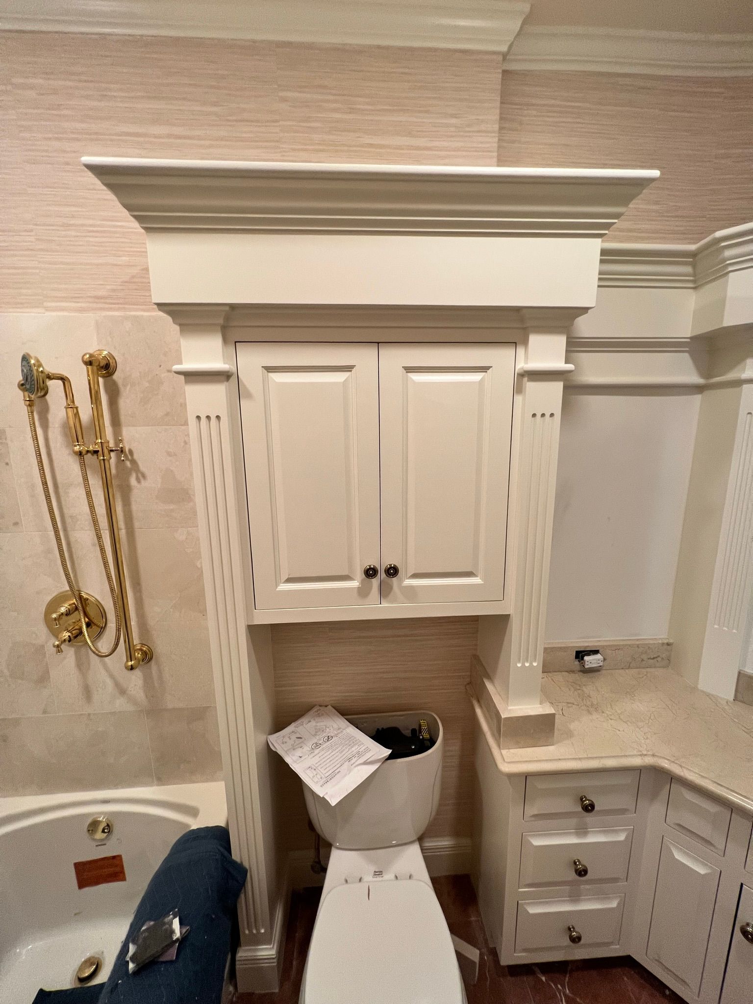 Bathroom with a toilet, cabinet above it, and adjacent vanity with drawers. Gold fixtures.