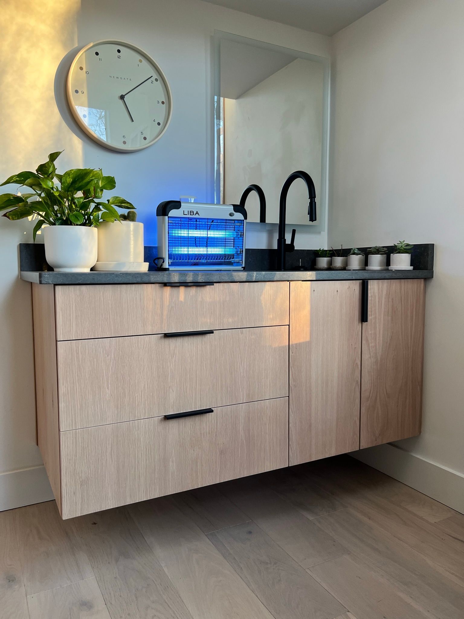Modern bathroom vanity with wood cabinet, black faucet, and round clock.