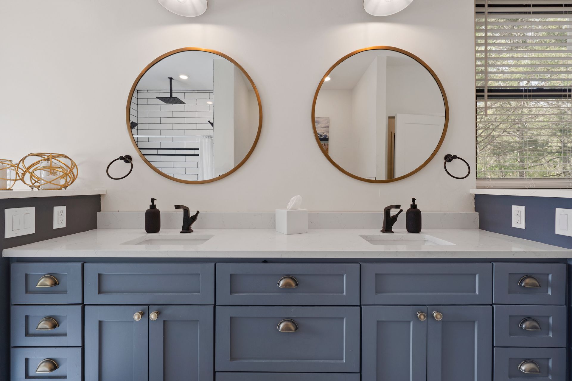 Bathroom vanity with blue cabinets, white countertop, two round mirrors, and black fixtures.