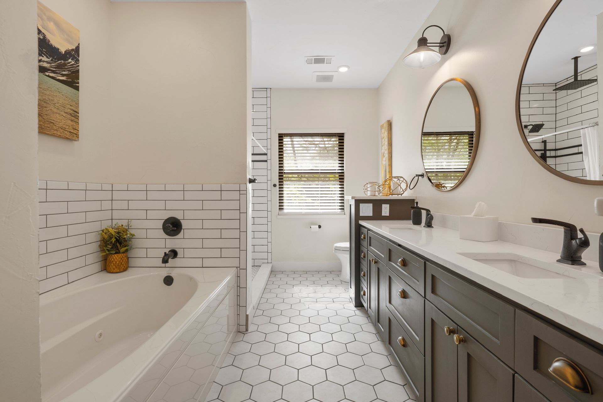 Bathroom with white and black tile, gray vanity, gold mirrors, and a window.