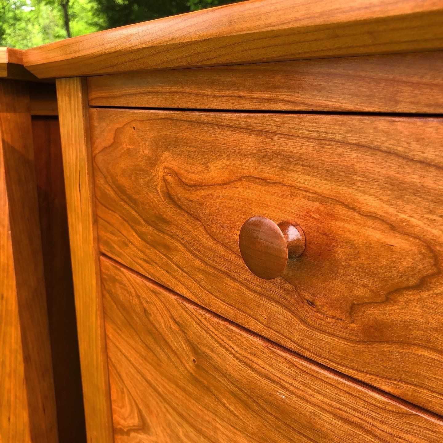 Close-up of a wooden dresser with a visible grain, a round knob, and a rich, reddish-brown finish.