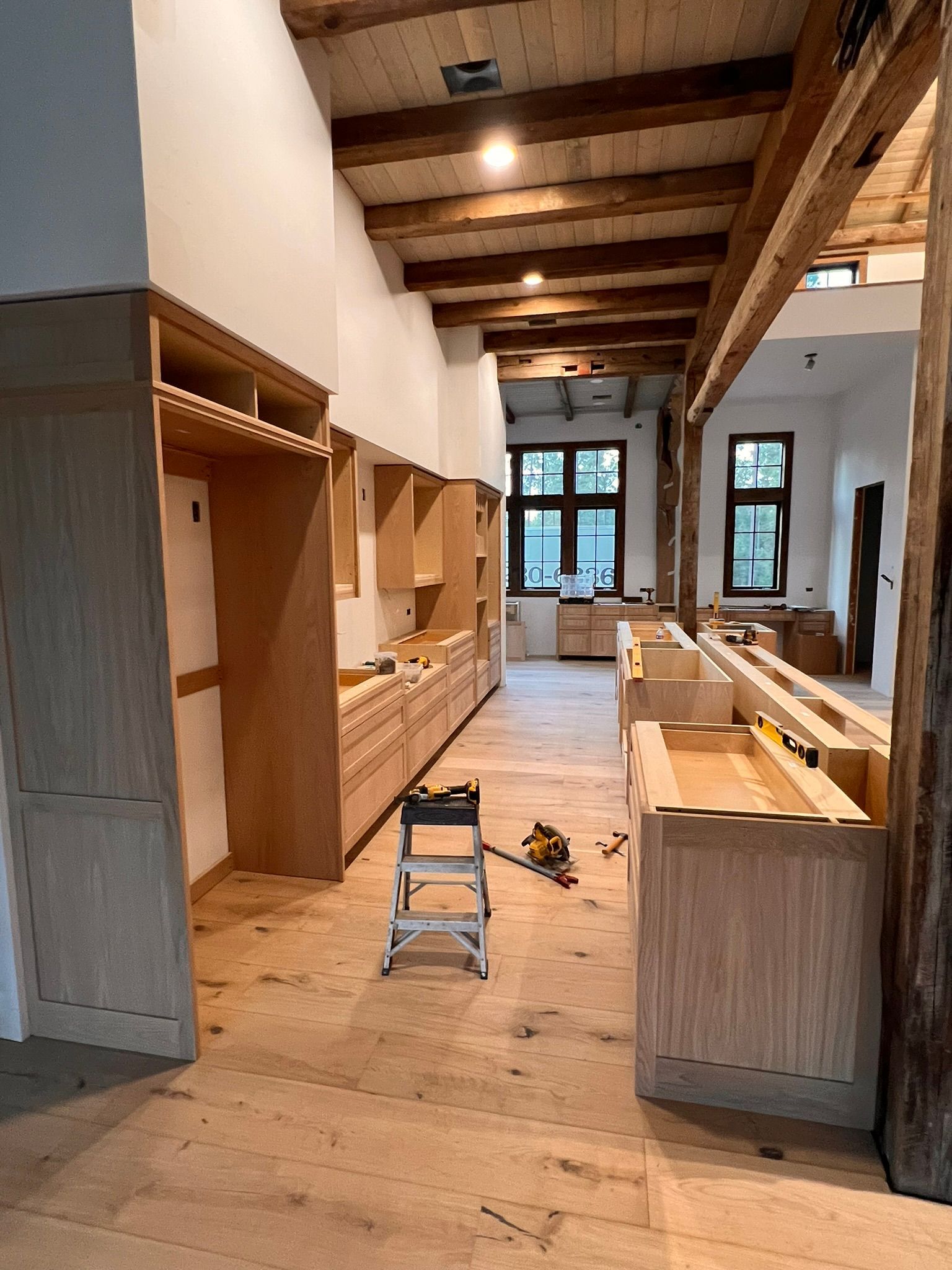 Interior of a kitchen under construction with light wood cabinets, wood beam ceiling, and a wooden floor.