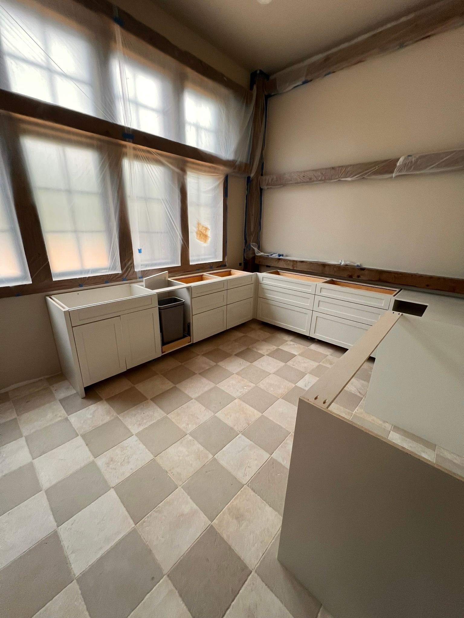 Kitchen under construction with white cabinets against a window, checkerboard floor.