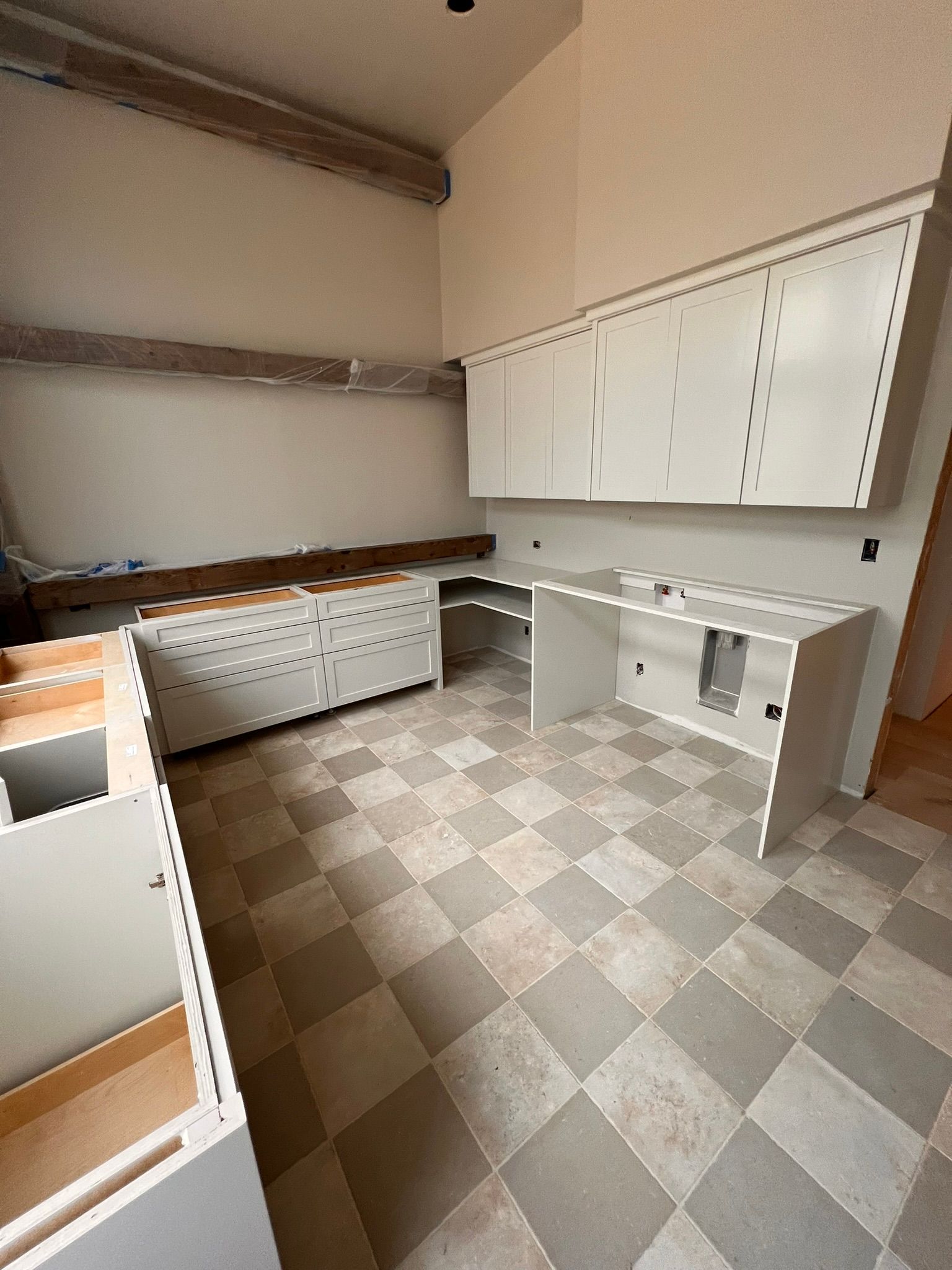 Unfinished kitchen with light cabinets and checkered floor.