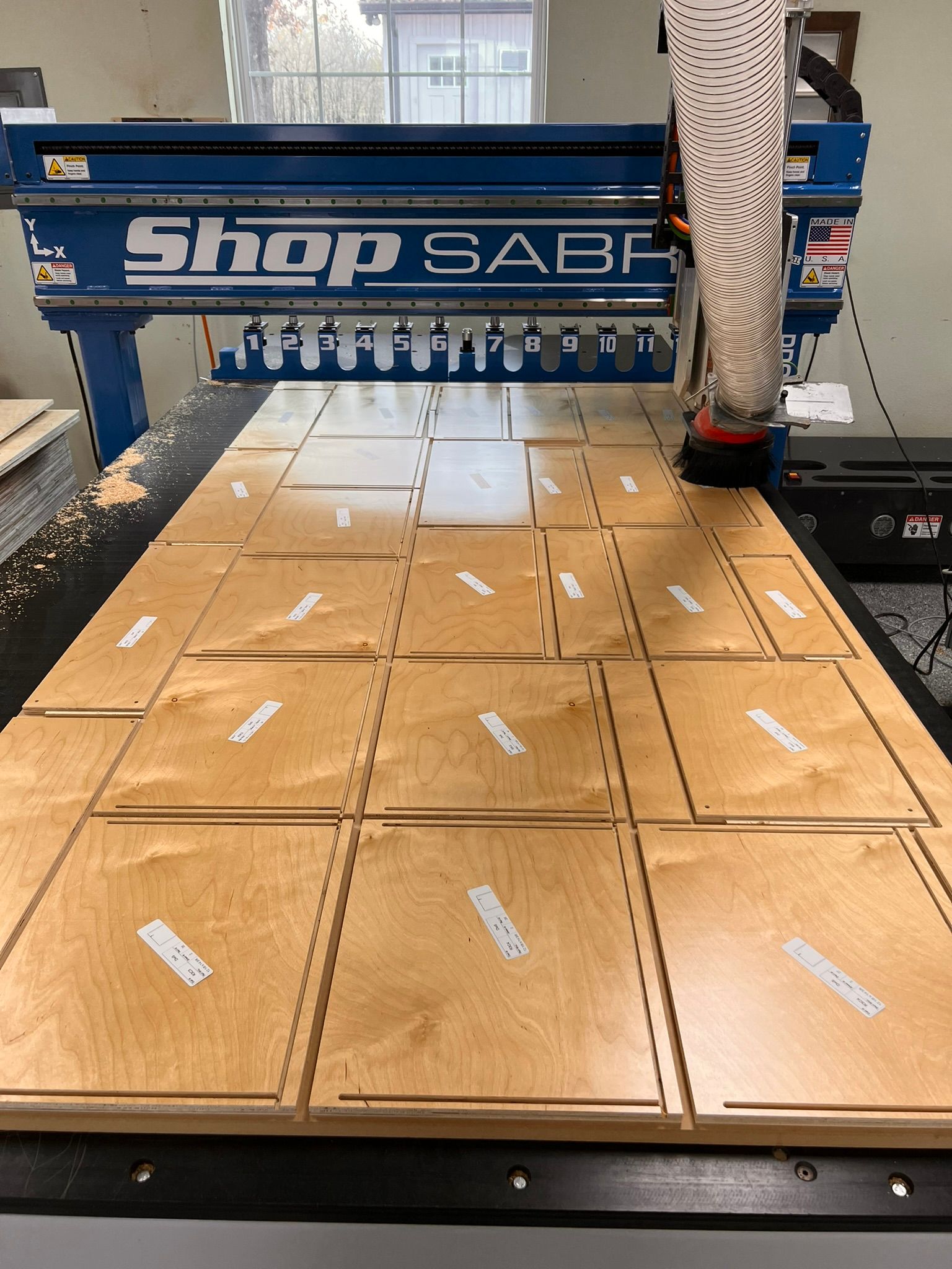 A CNC router (ShopSabre) cutting shapes from plywood sheets. Several cut pieces are visible on the machine bed.
