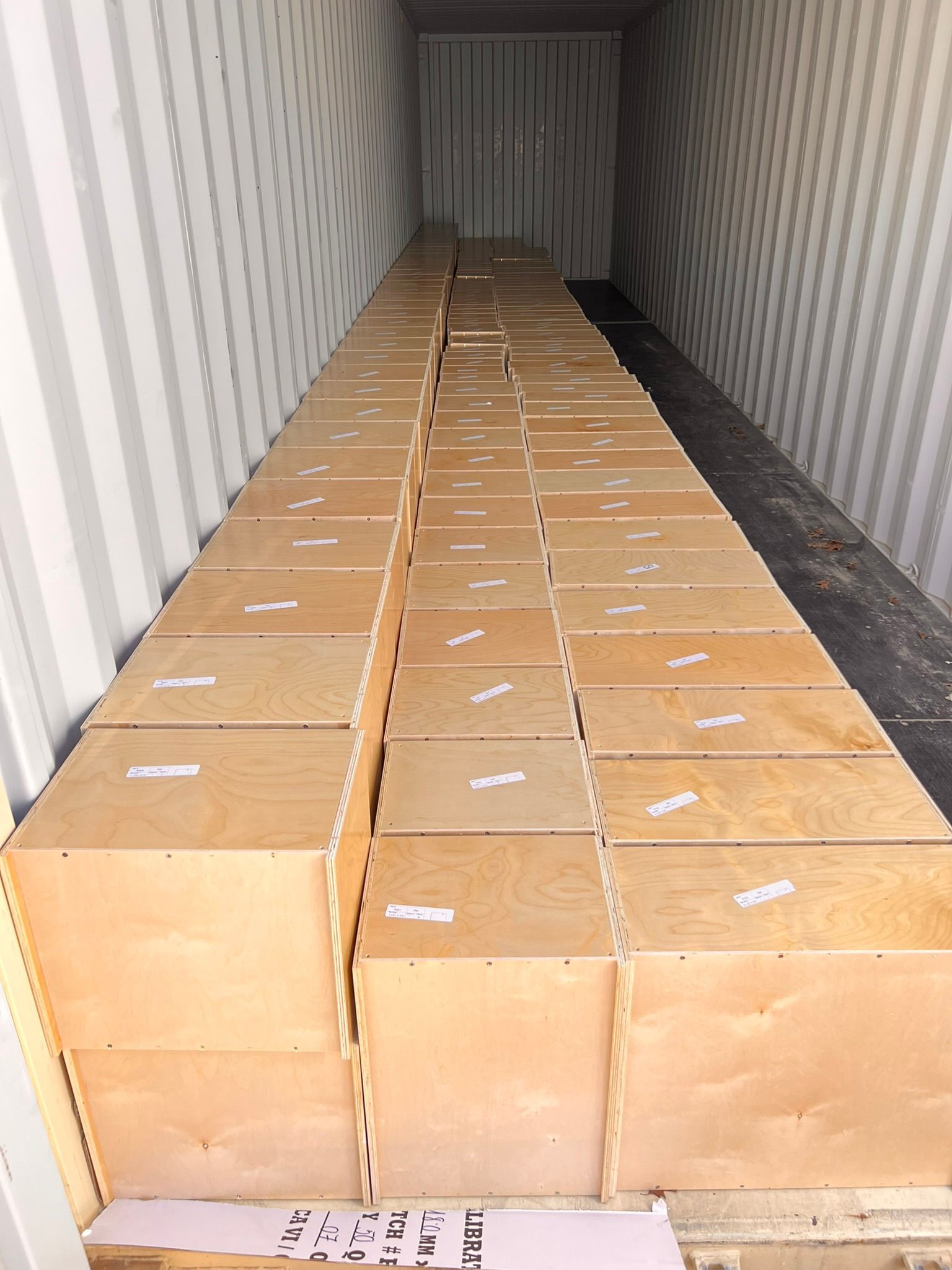 Boxes stacked inside a shipping container. Light-colored wood boxes with labels are tightly packed.