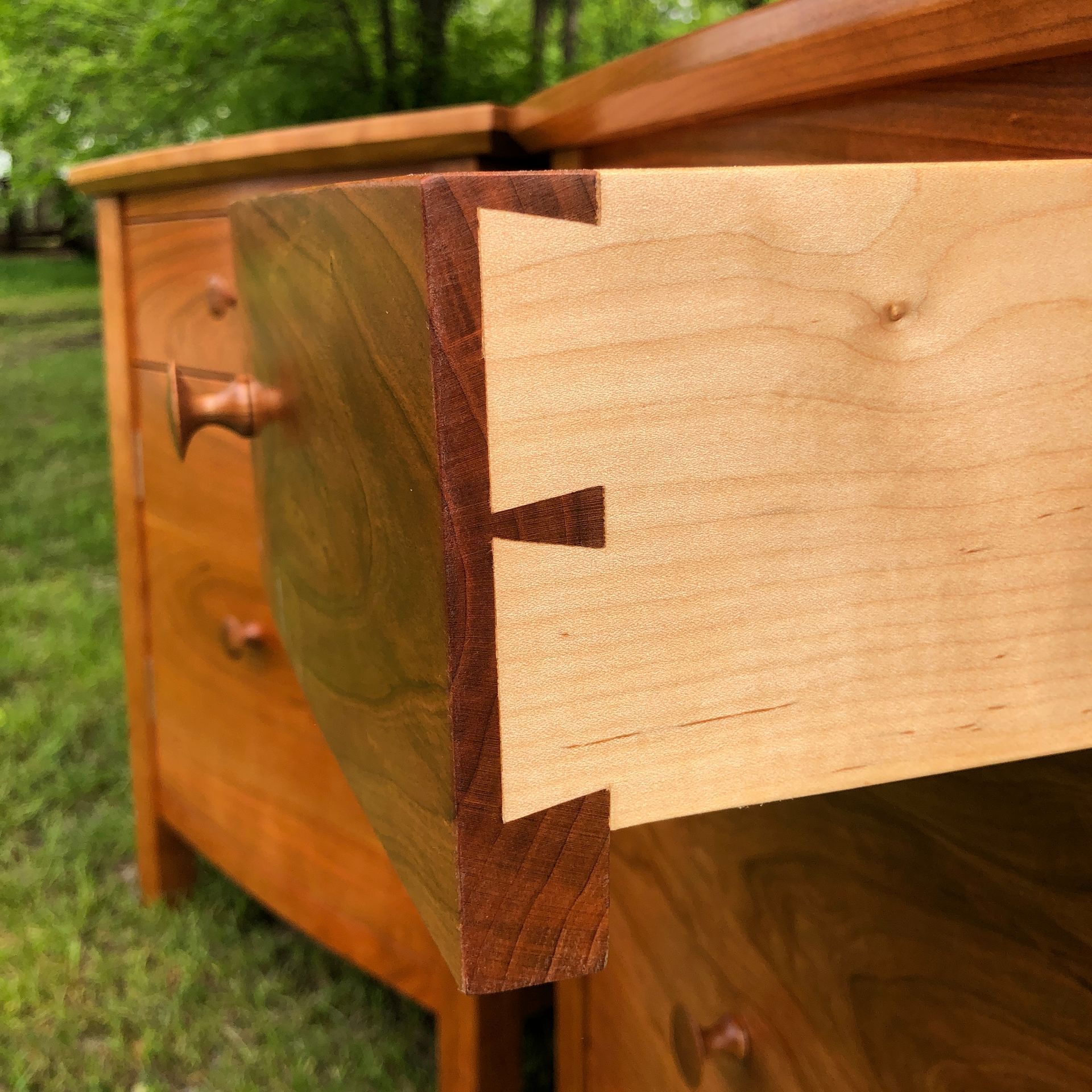 Wooden drawer, open, showing dovetail joints, in a cherry wood chest of drawers, outdoors.