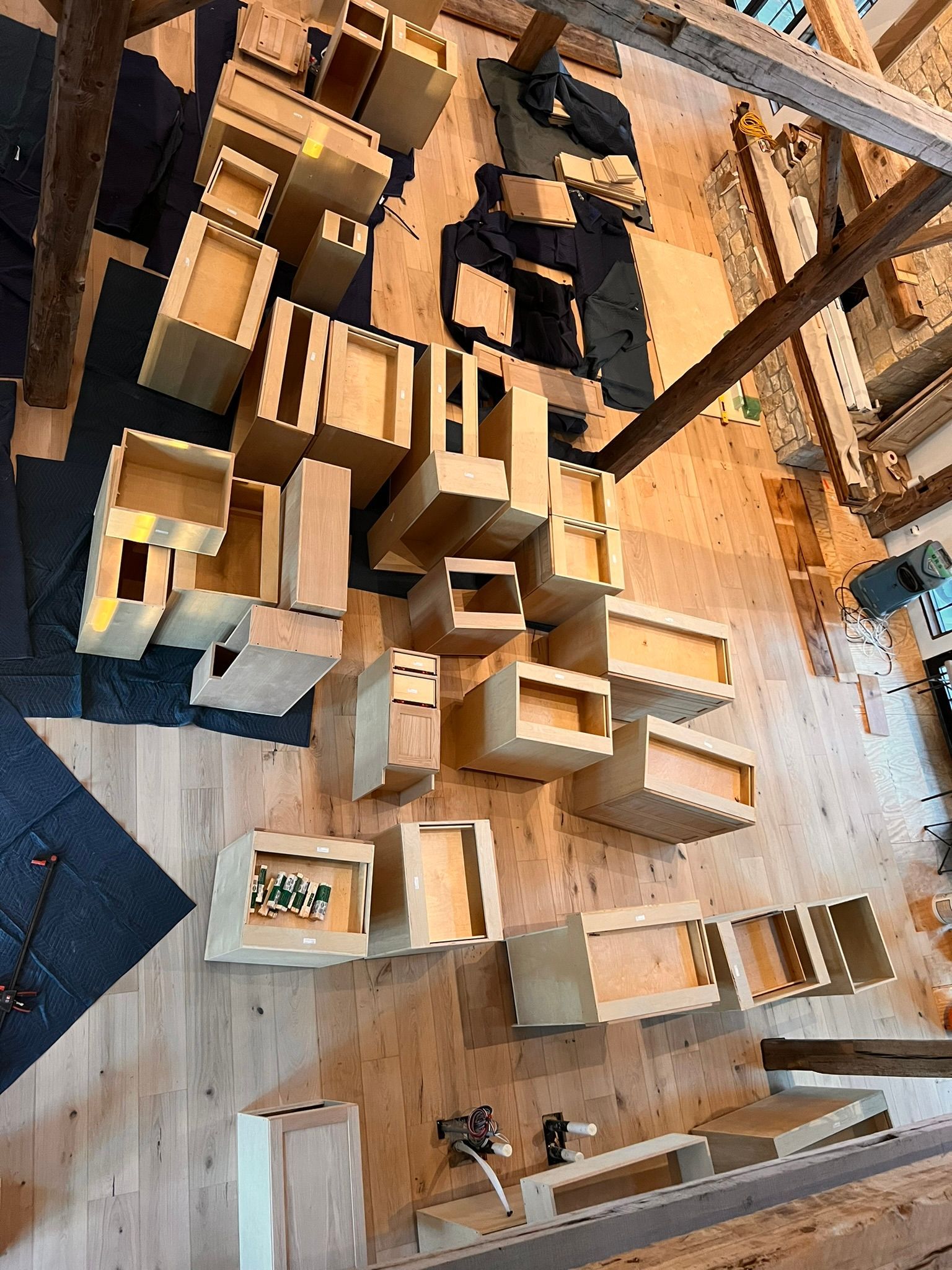 Wooden drawer boxes scattered on a wooden floor, under exposed beams, near a partially covered surface.