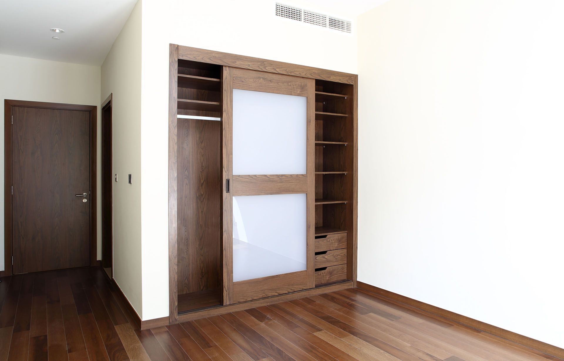 Empty room with wood floor and a large wooden wardrobe against the wall.