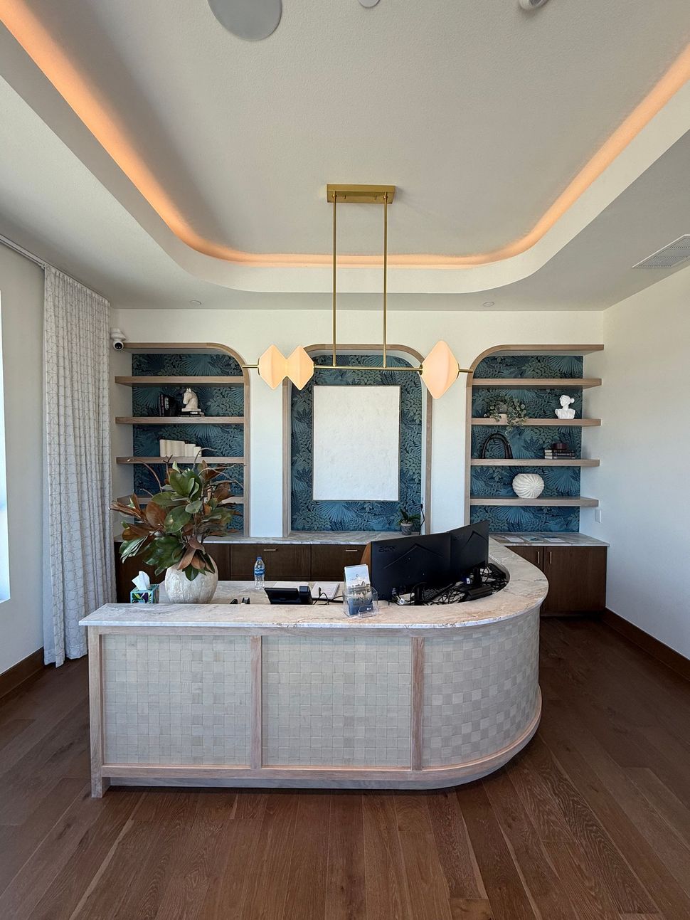 Modern reception desk in a bright office with teal shelving, mirrors, and warm recessed ceiling lights