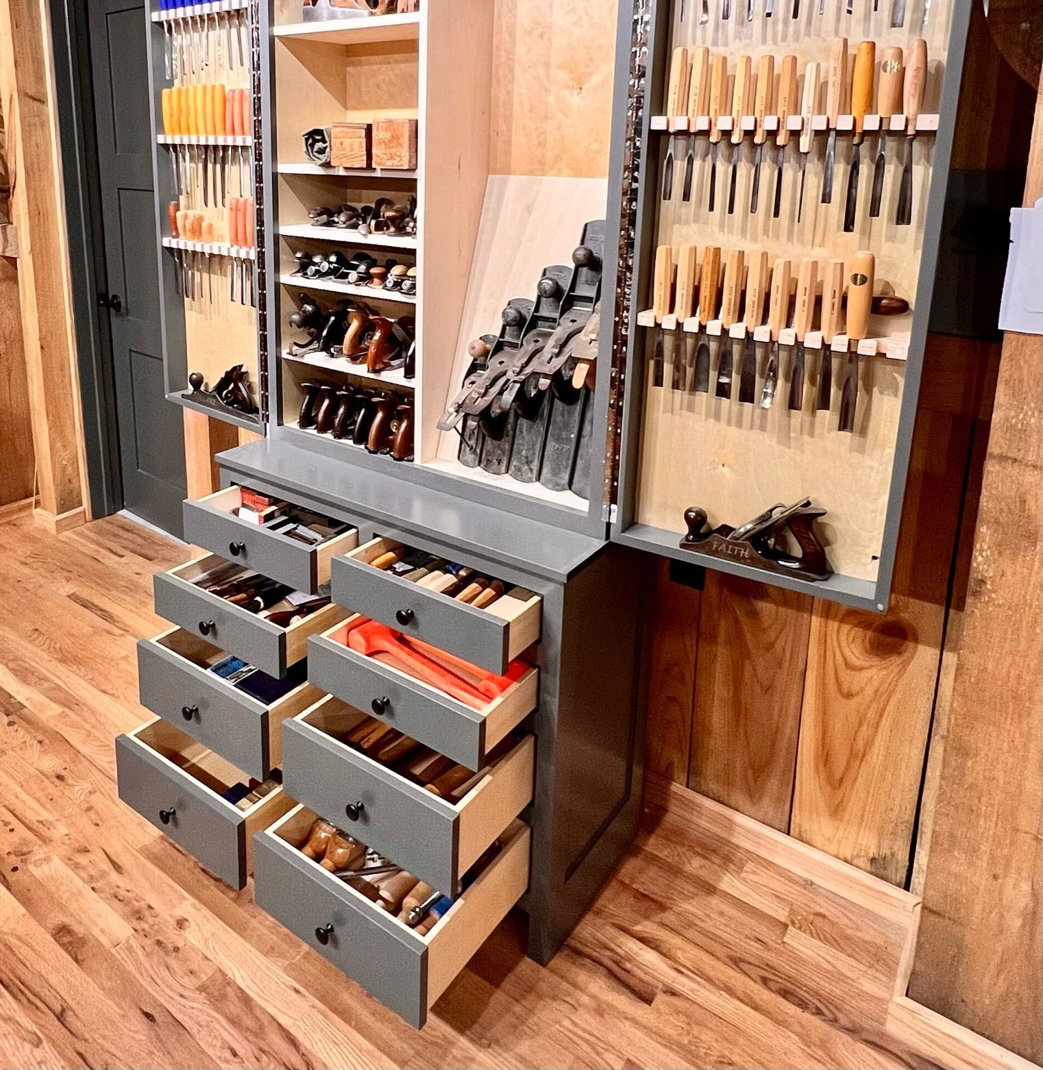 A gray woodworking tool cabinet with open drawers and doors, revealing a variety of tools.