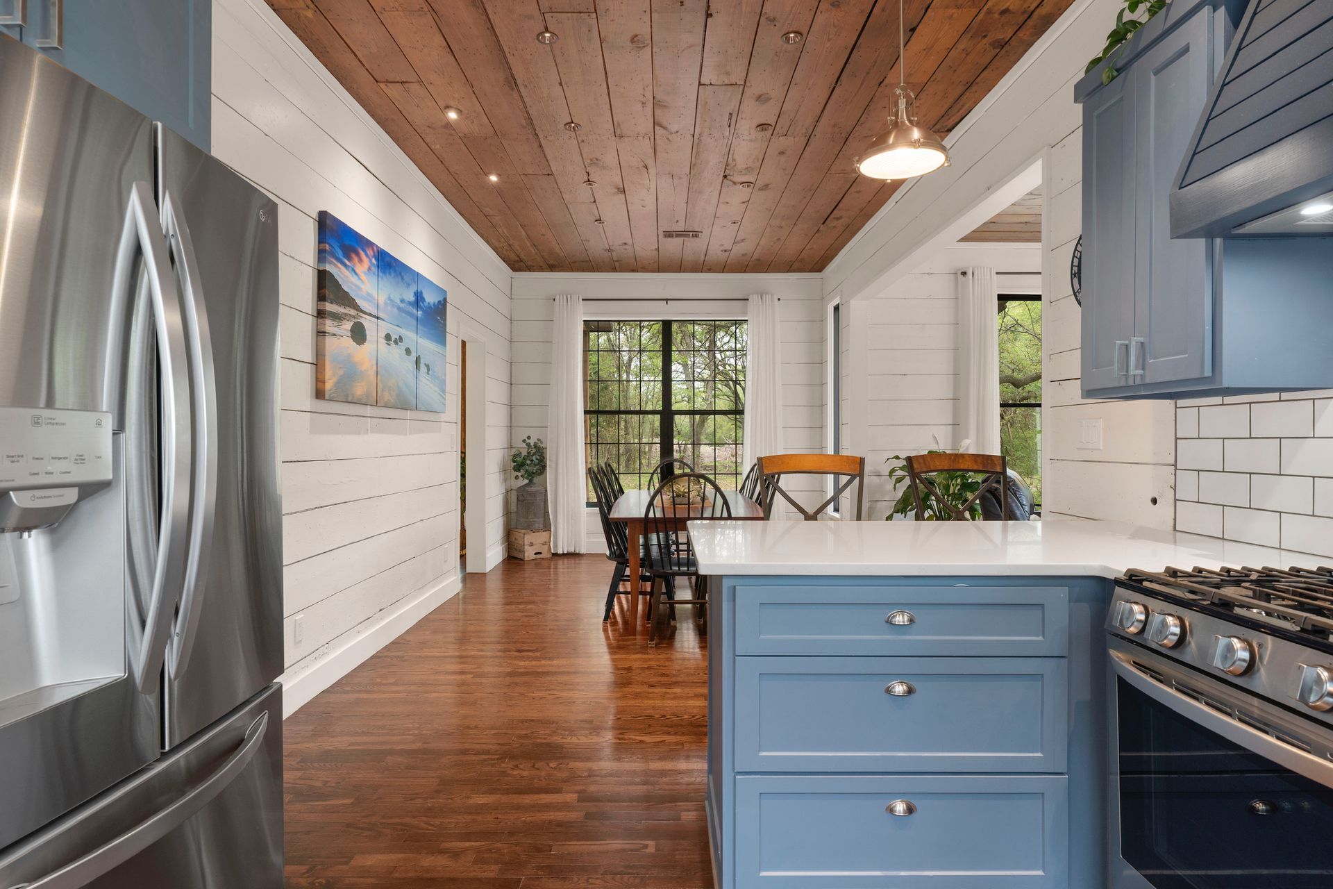 Kitchen with blue cabinets, stainless steel refrigerator, and wood ceiling and floors.
