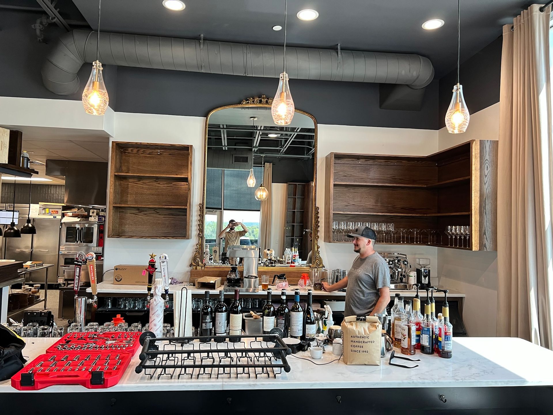 Bar interior with a bartender, bottles, and liquor. Overhead lights and a decorative mirror are visible.