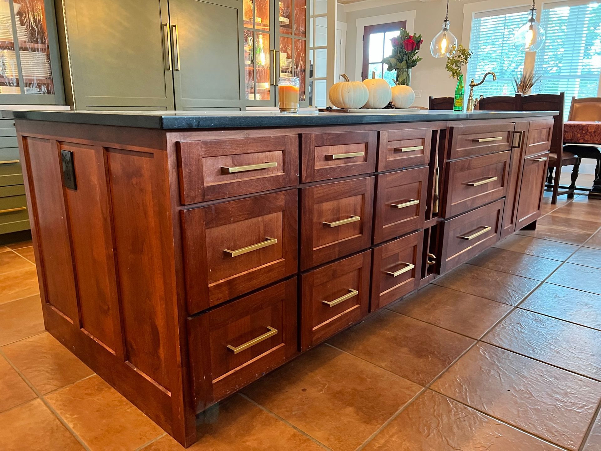 Kitchen island with dark wood cabinets, black countertop, gold hardware.