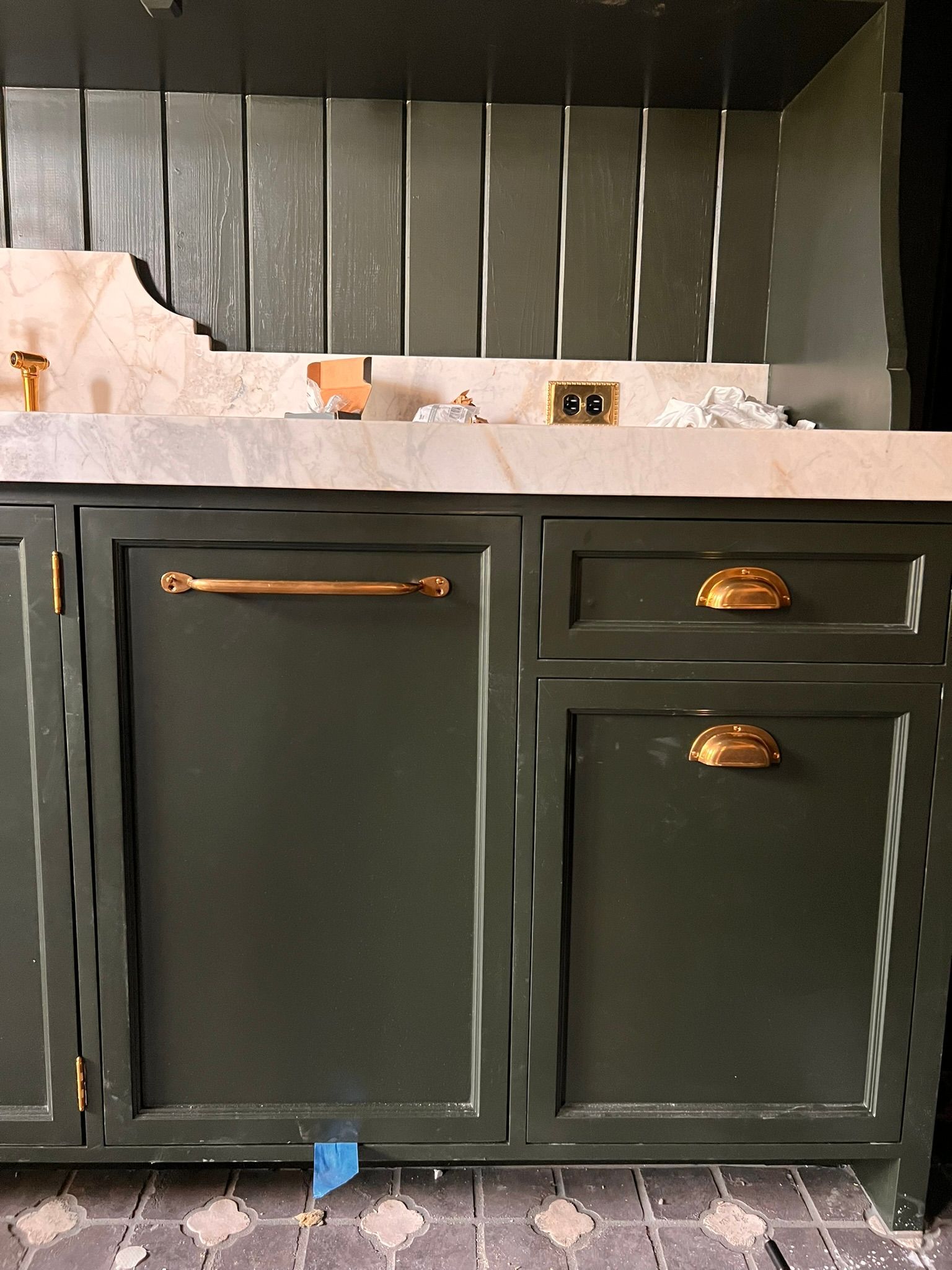 Dark green cabinets with gold hardware in a kitchen, against a backsplash, and vertical paneling.