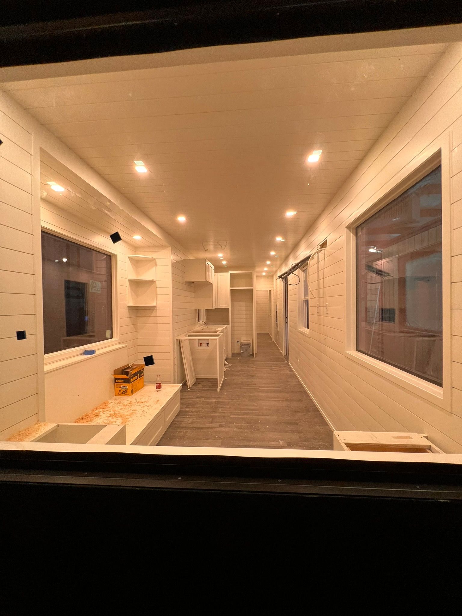 Interior of a room under construction with white walls, wood floors, and windows.