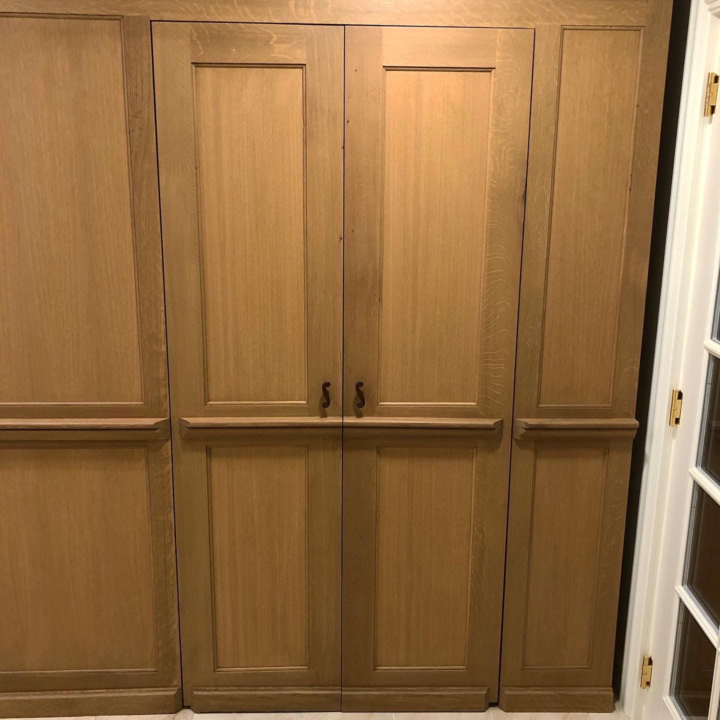 Wooden built-in closet with four doors. The closet is oak-colored and has simple black hardware.
