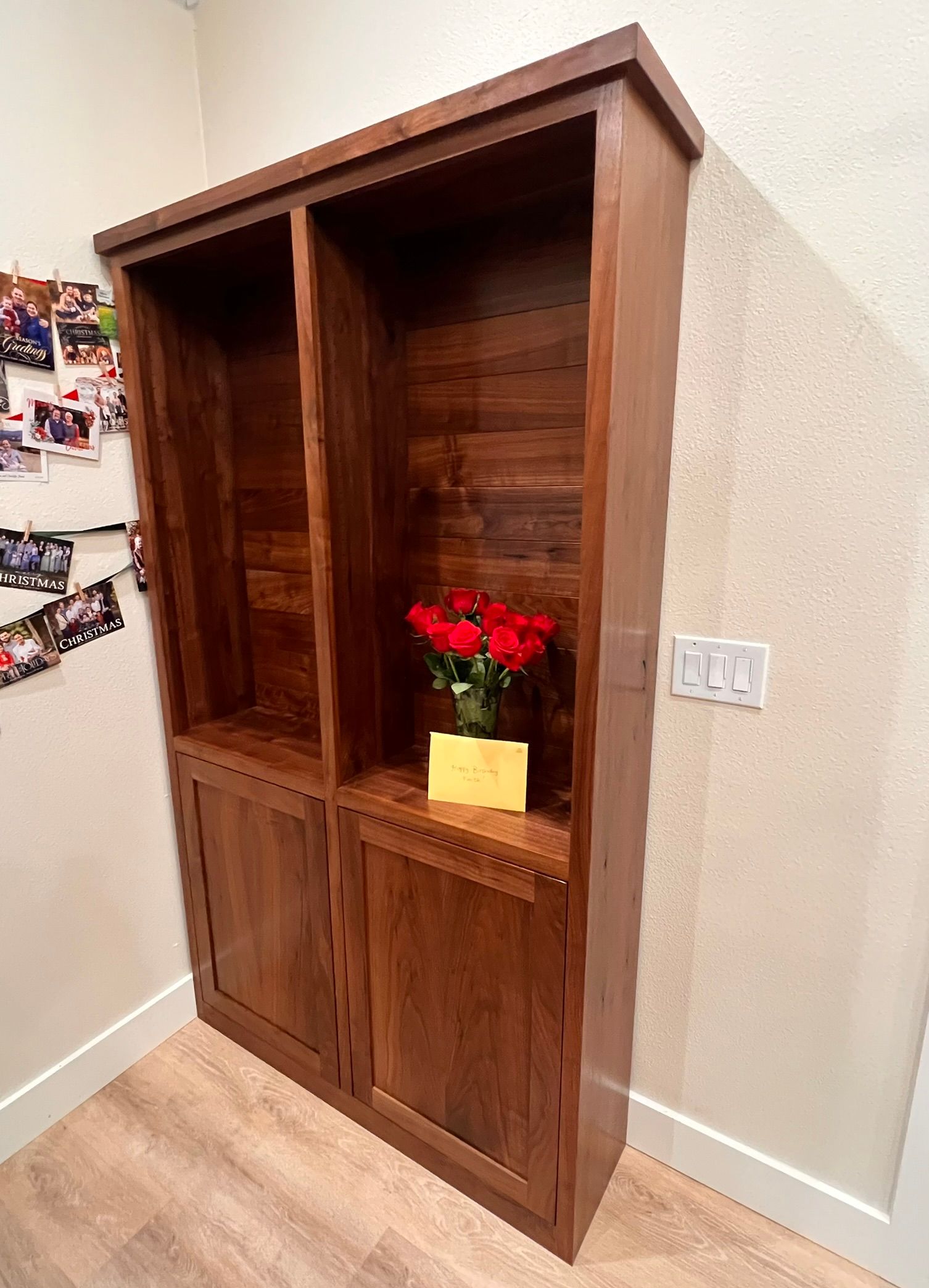 Wooden cabinet with two open upper sections and two lower cabinet doors; red roses on shelf.