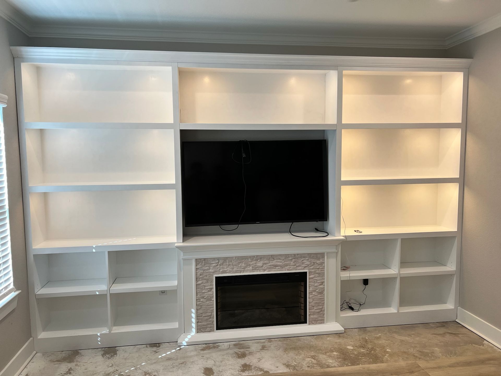White built-in entertainment center with shelving, a fireplace, and a centered television.