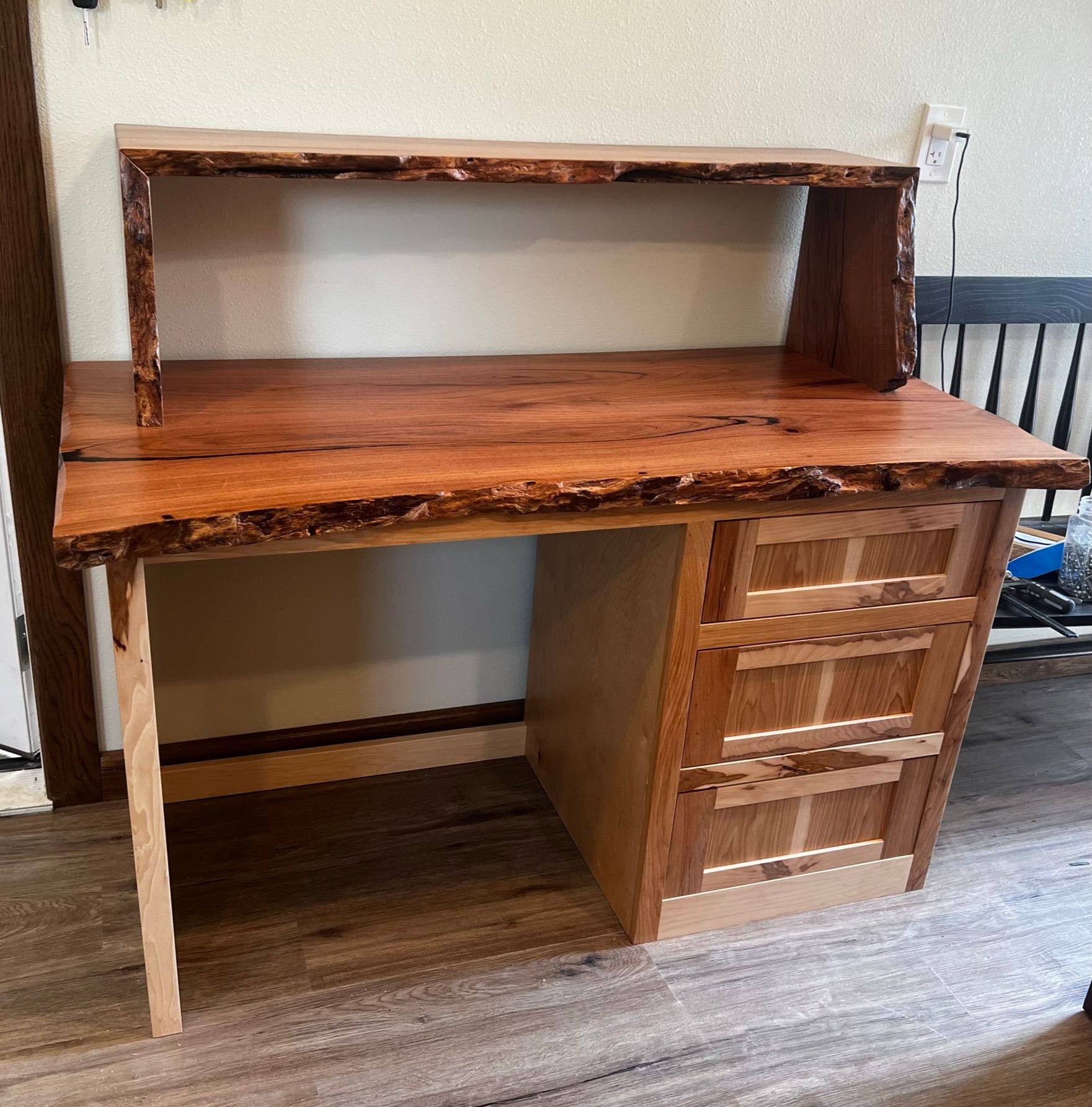Wooden desk with live edge desktop and hutch, drawers on right, light wood legs.