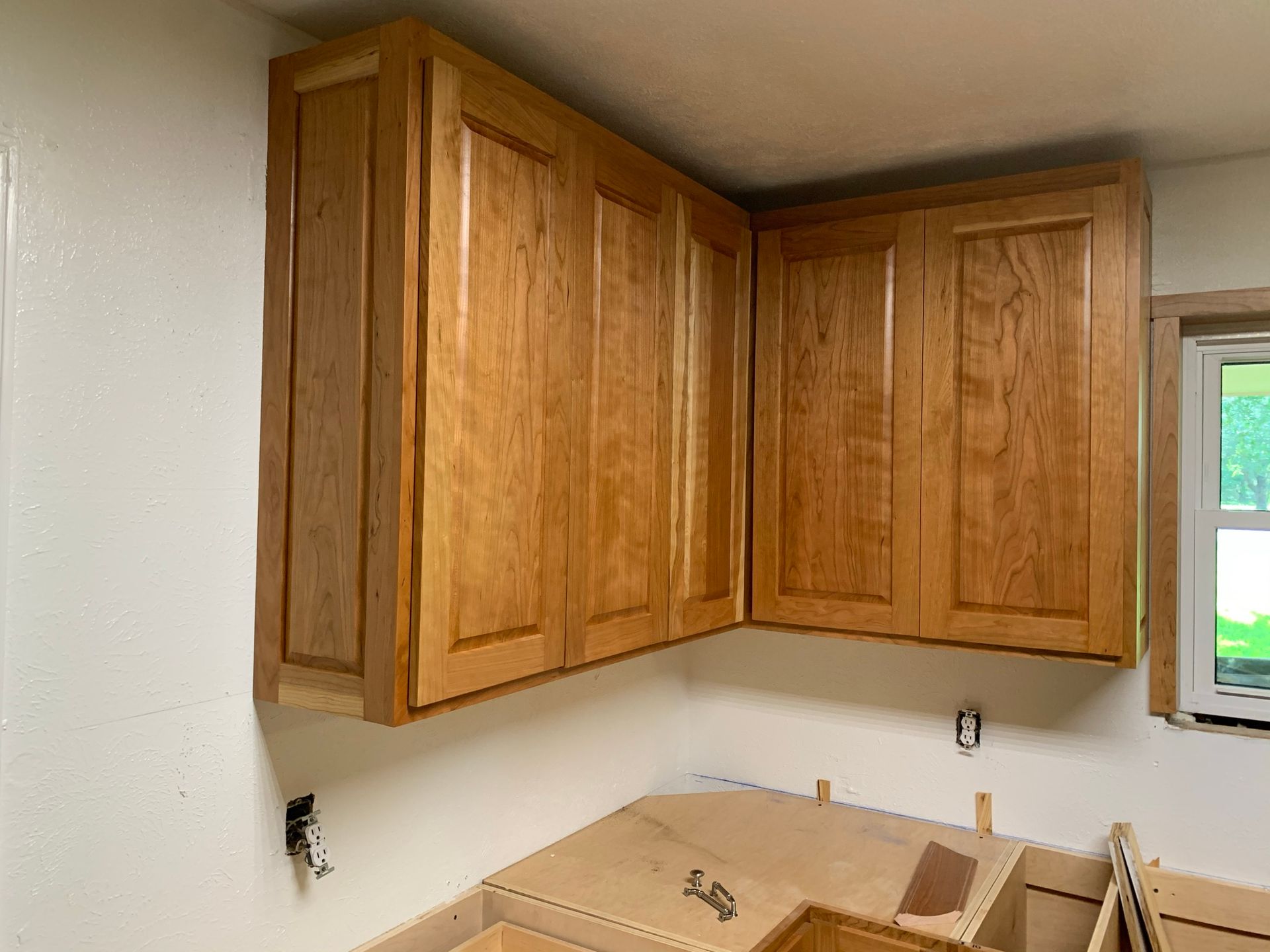 Wooden kitchen cabinets installed on a wall corner; unfinished lower cabinets below.