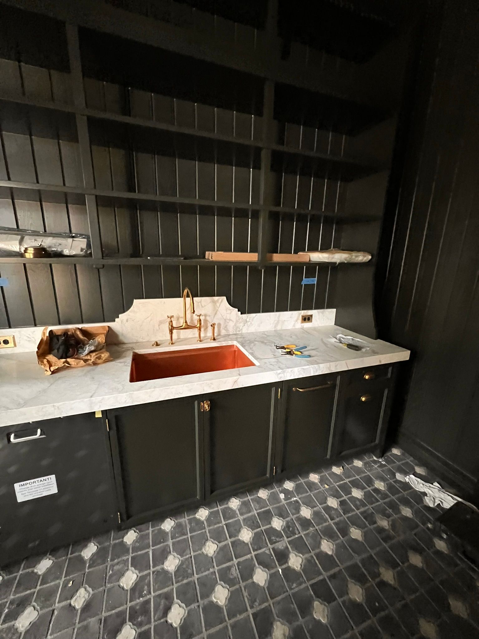 Dark cabinetry and shelves with a copper sink, white countertop, and patterned tile floor.