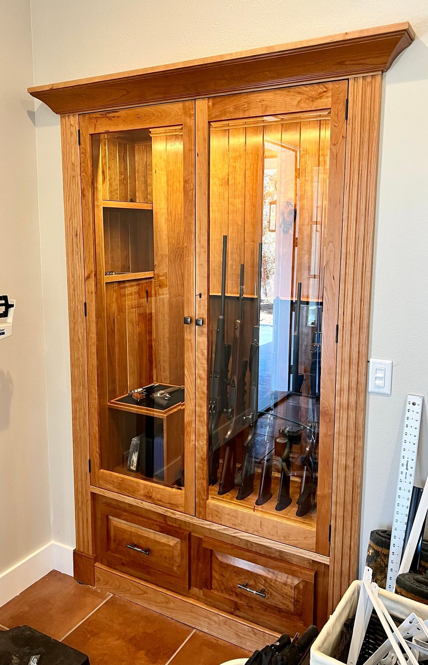 Wooden gun cabinet with glass doors, illuminated interior, and drawers.