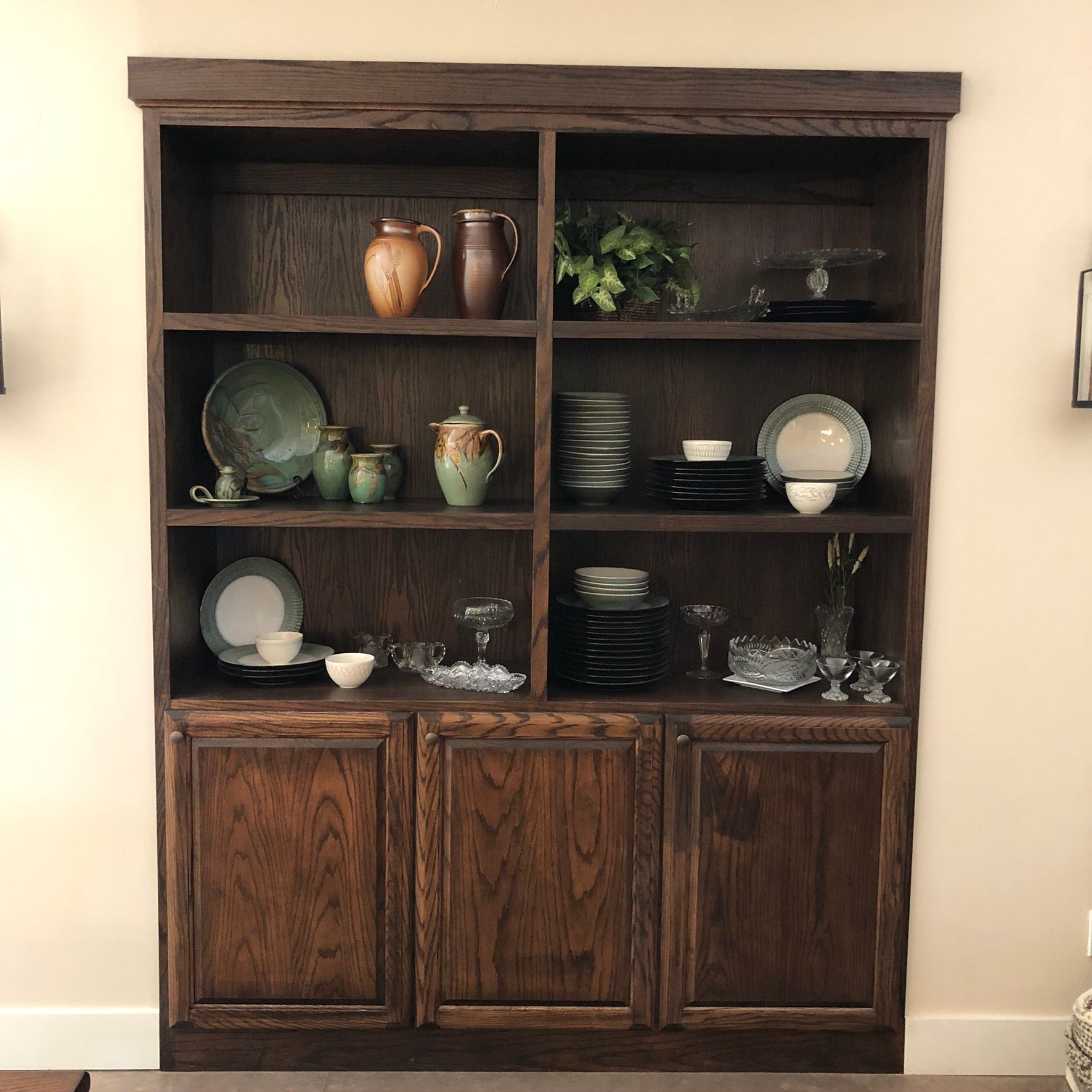 Wooden cabinet with dishes, jugs, and plants in a room.