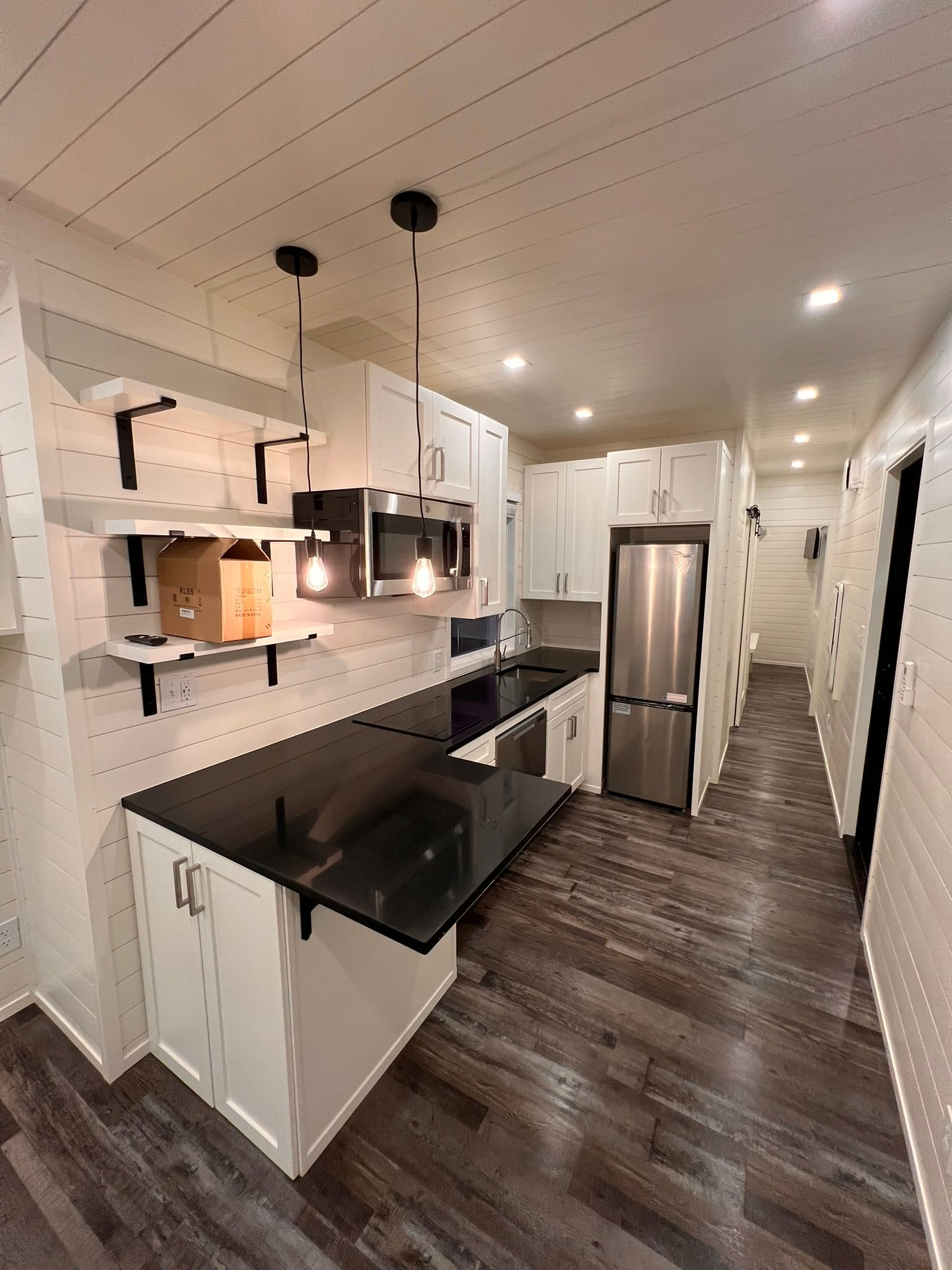 Modern kitchen with white cabinets, black countertops, stainless steel appliances, and wood flooring.