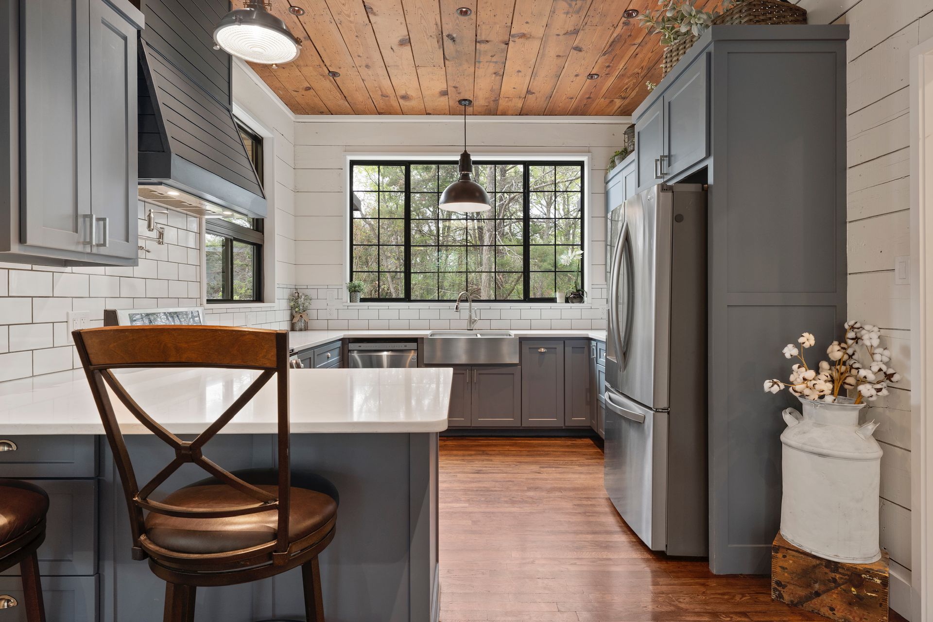 Kitchen with blue cabinets, wood ceiling, white countertops, and a large window.