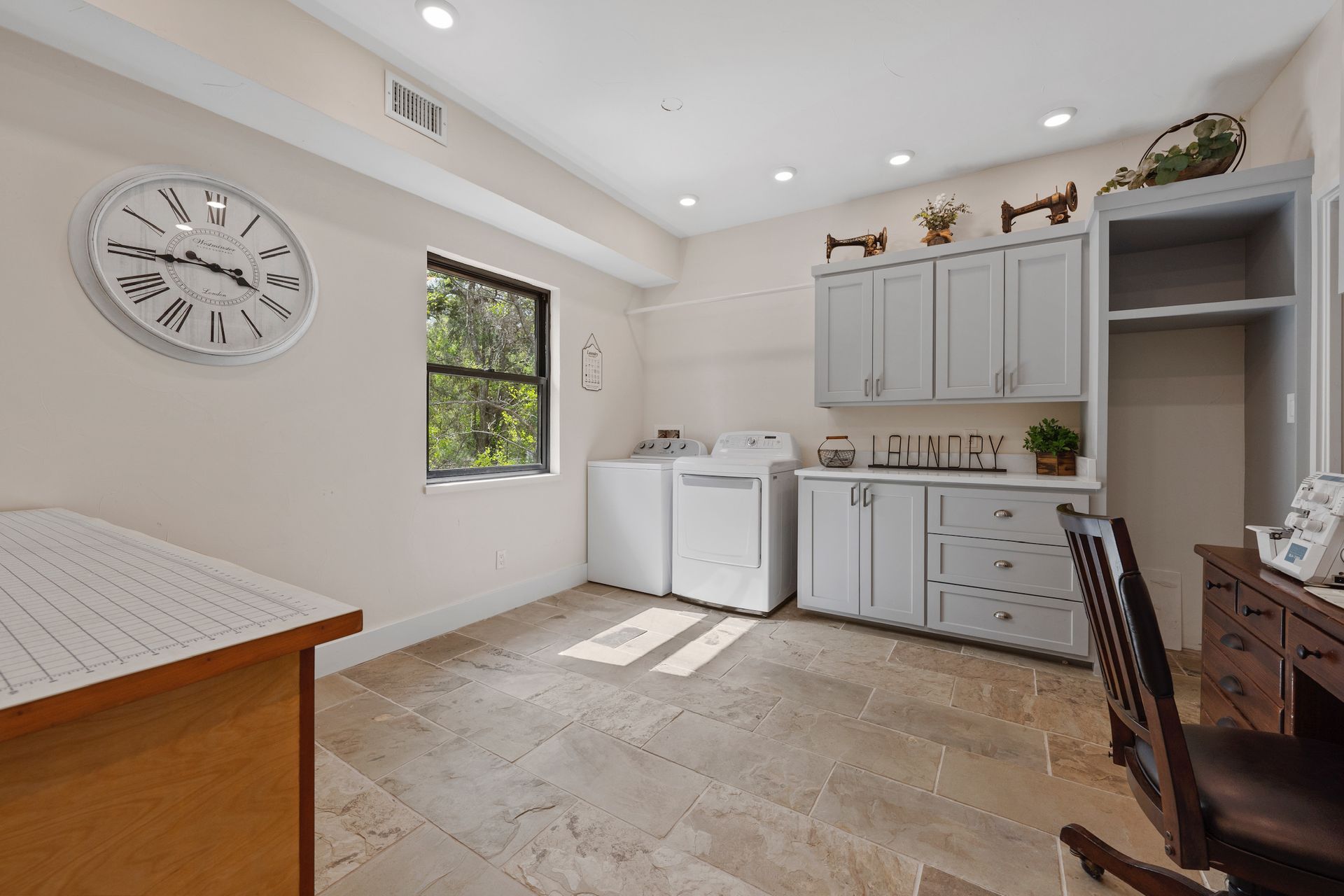 Laundry room with washer, dryer, cabinets, sink, desk, and clock. Beige and gray color scheme.