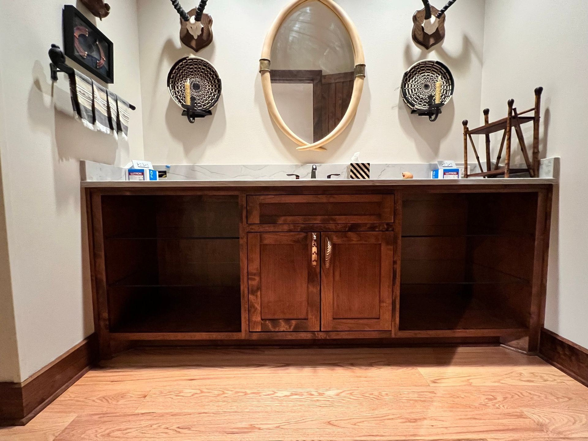 Wooden vanity with oval mirror, cabinets, and decorative wall mounts in a room with hardwood flooring.