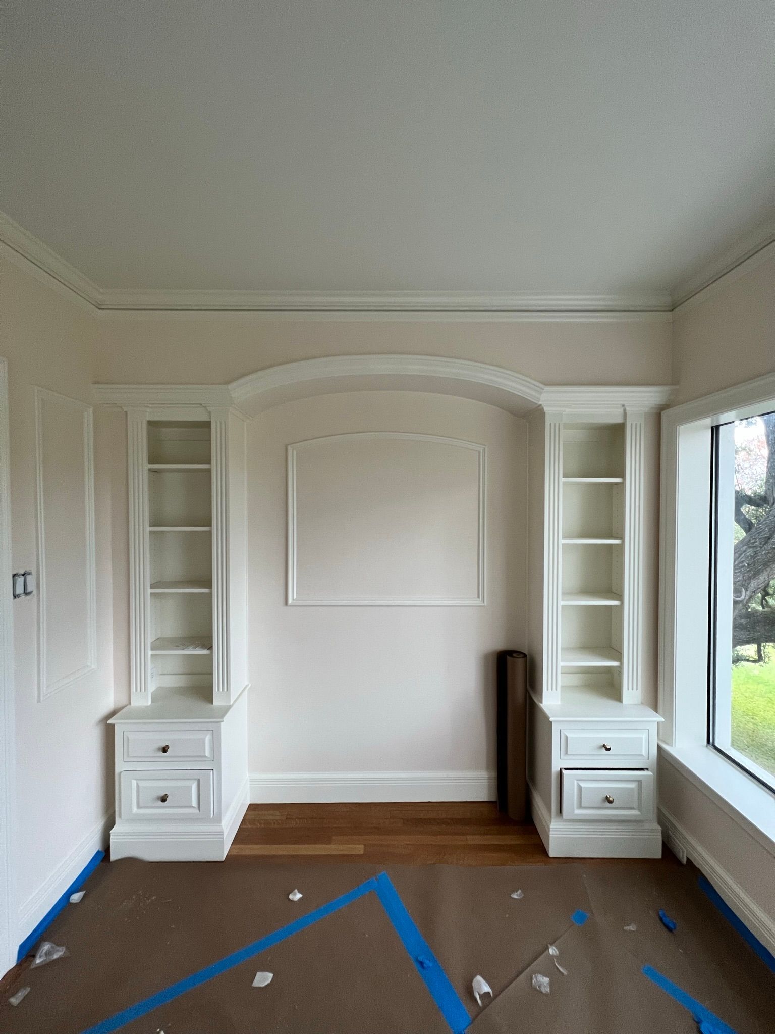 Built-in white bookshelves with cabinets frame a central wall panel beneath an arched ceiling detail.