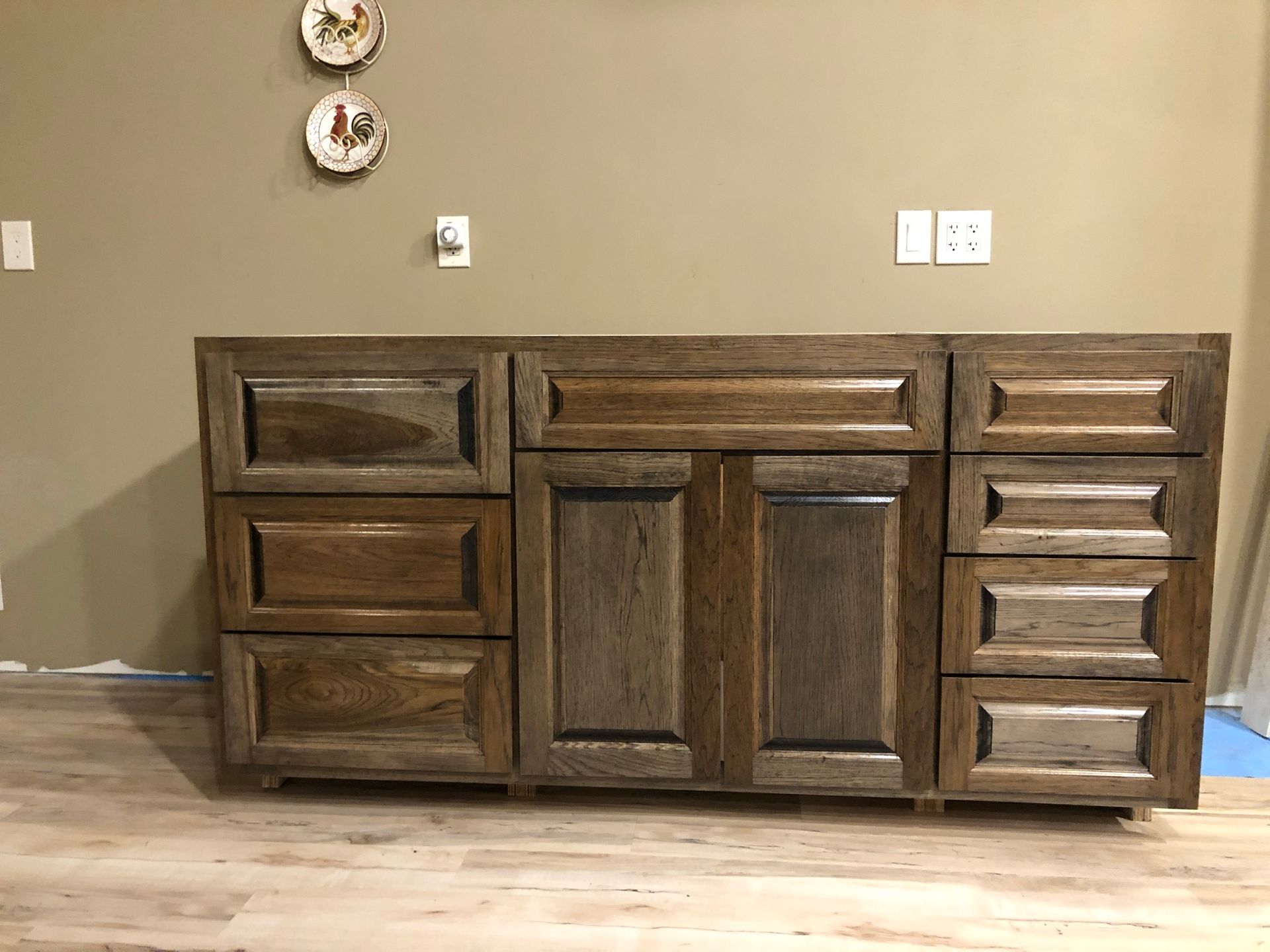 Wooden bathroom vanity with drawers and doors, installed against a beige wall, on a wood-look floor.
