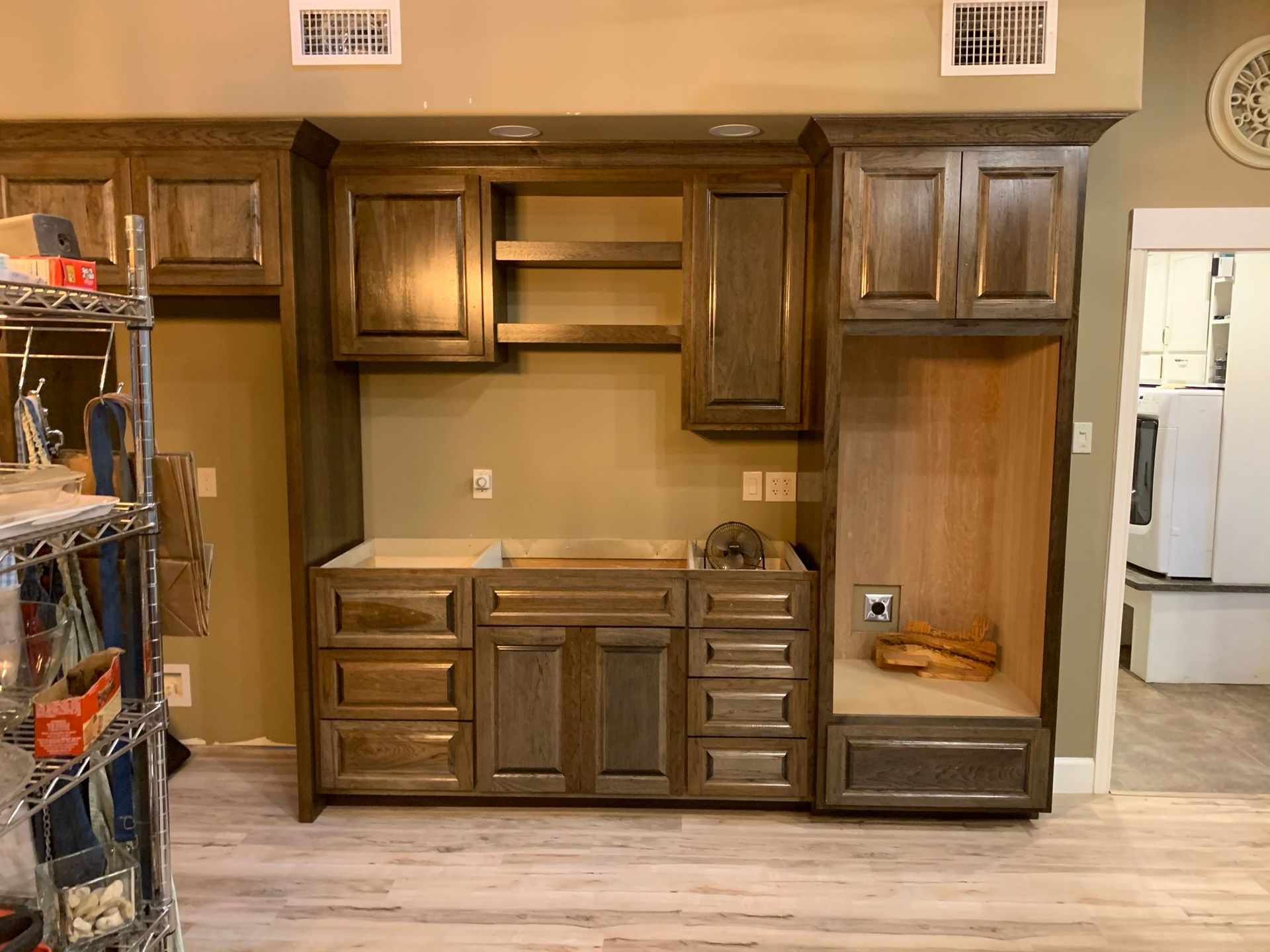 Wooden kitchen cabinets, unfinished, against a tan wall, and light wood floor.