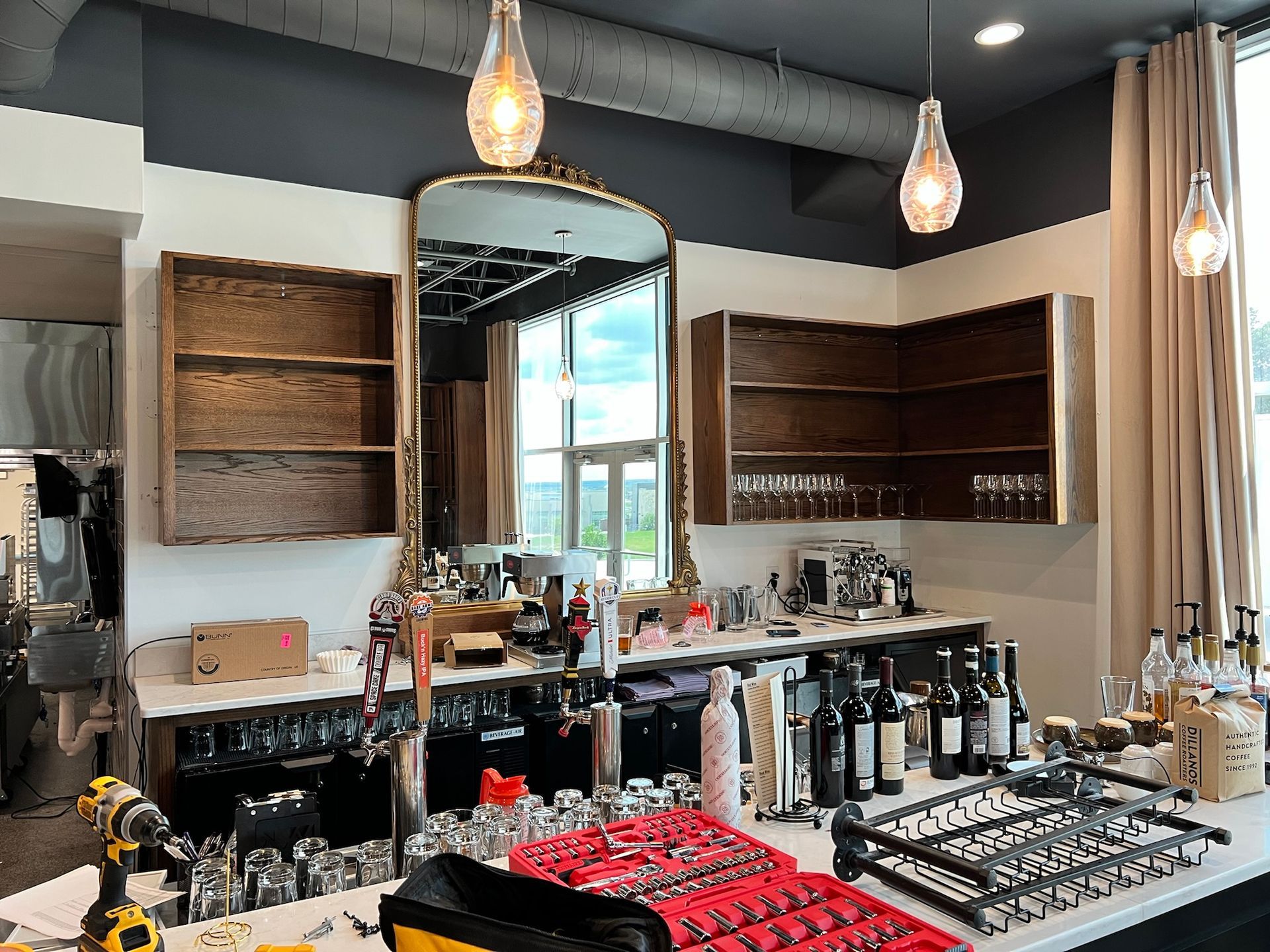Bar interior with mirror, shelving, bottles, and tools on counter.