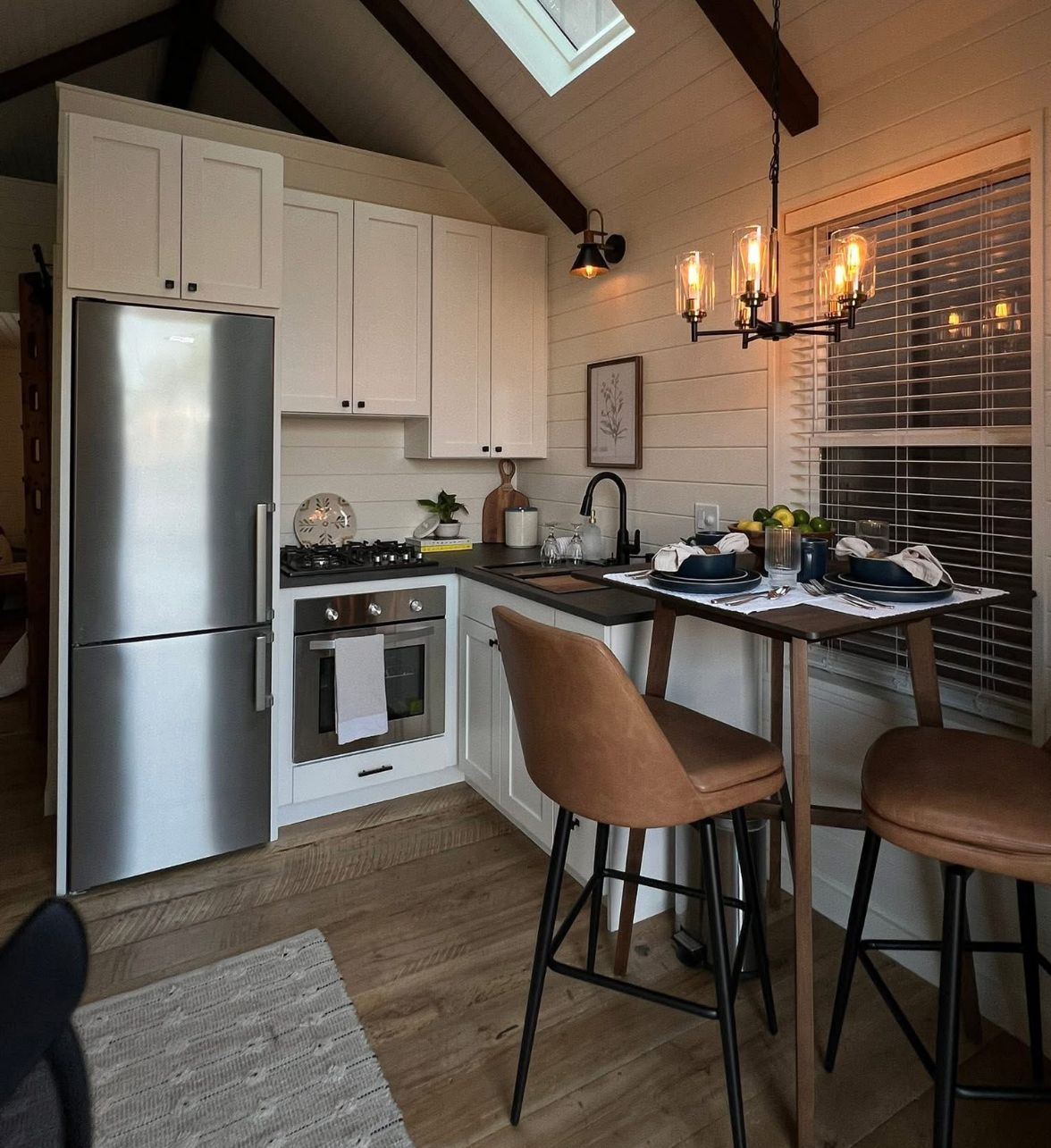 Small kitchen with stainless steel refrigerator, white cabinets, and a bar table with stools.