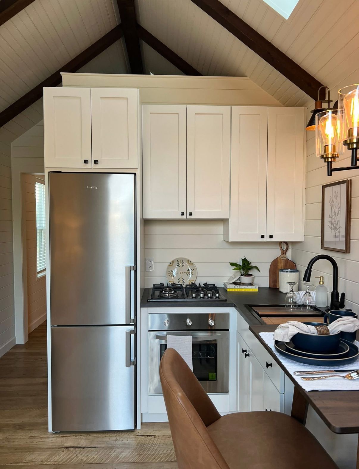 Small kitchen with white cabinets, stainless steel fridge, and small oven, featuring a table with a plate.
