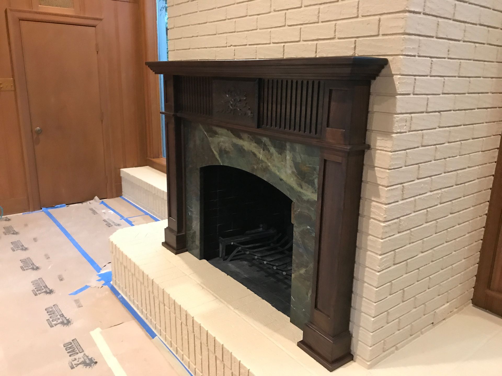 Fireplace with dark wooden mantel, green marble surround, and beige brick facing.