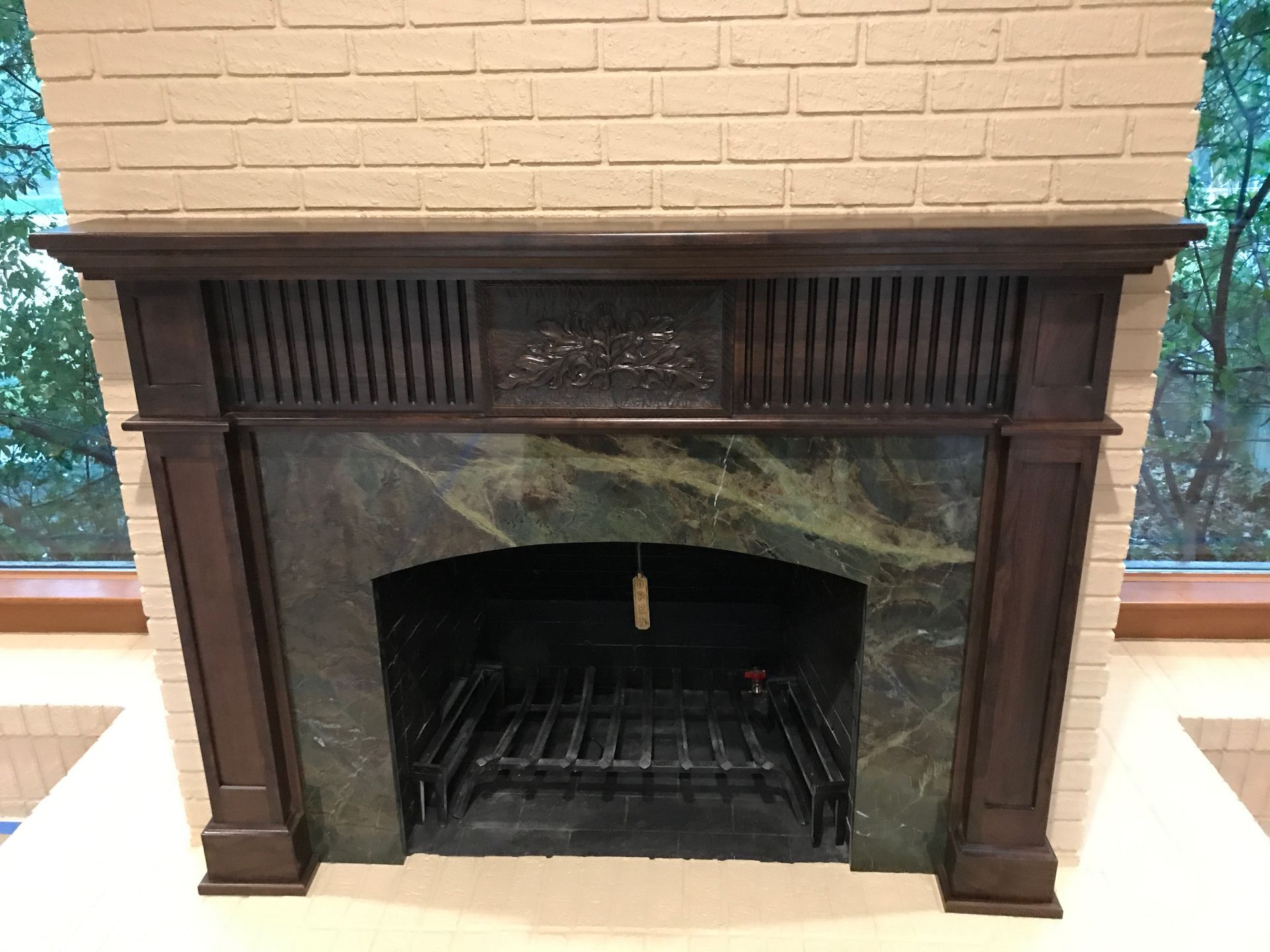Fireplace with green marble surround, dark wood mantel, brick background.