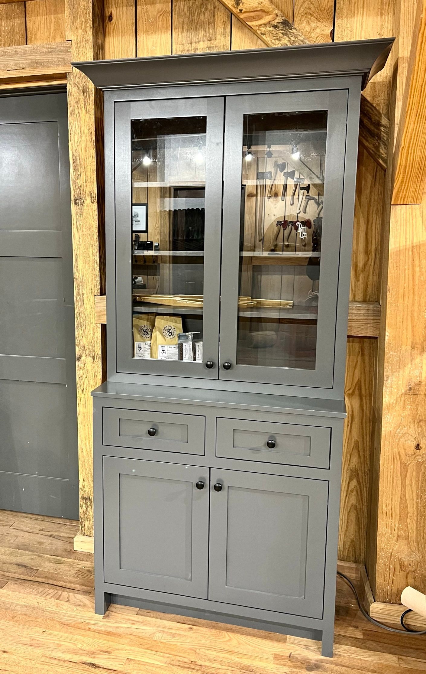 Gray painted cabinet with glass doors, set against a wood background.