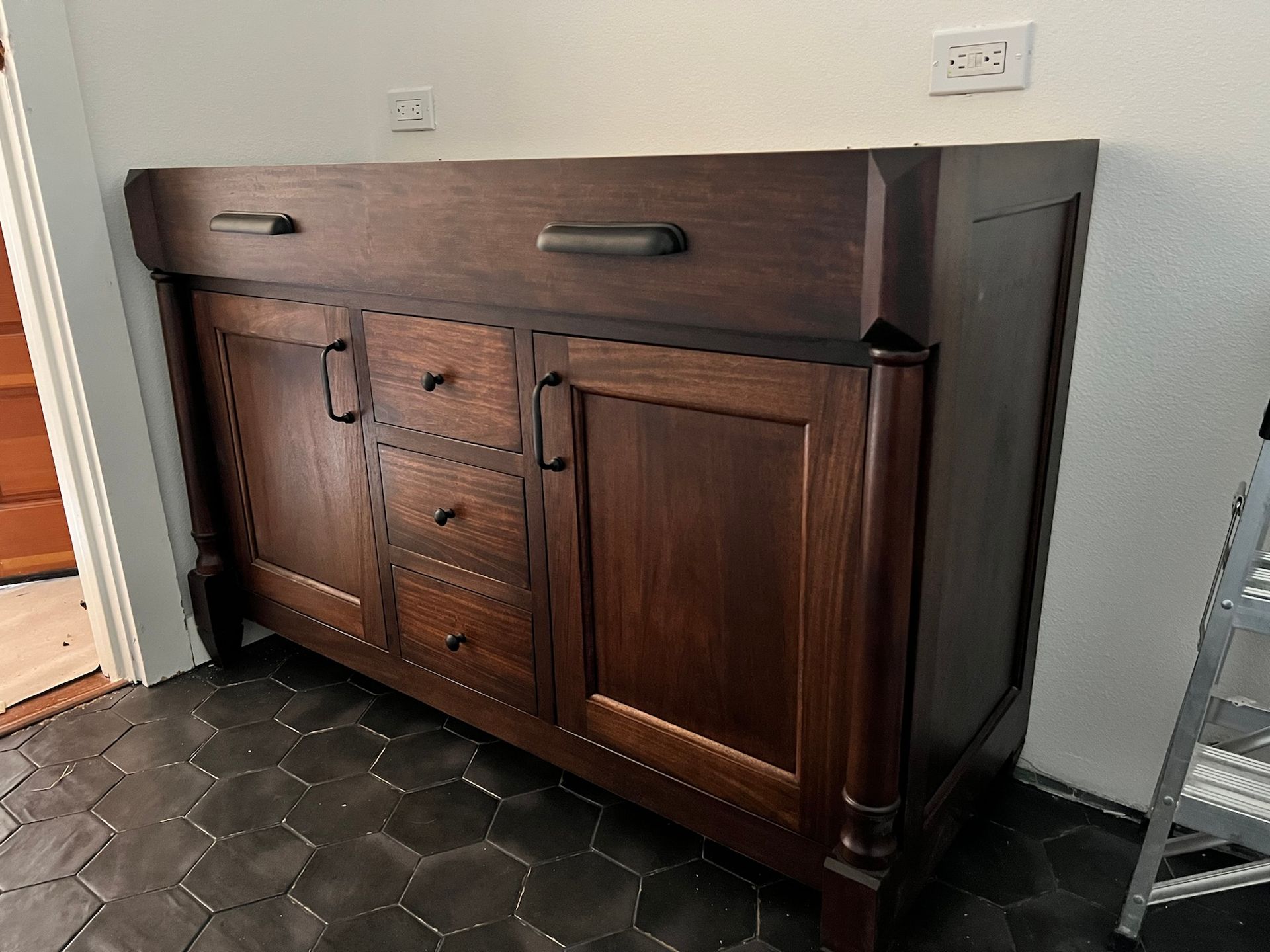 Dark wood cabinet with drawers and doors, black handles, set against a white wall.