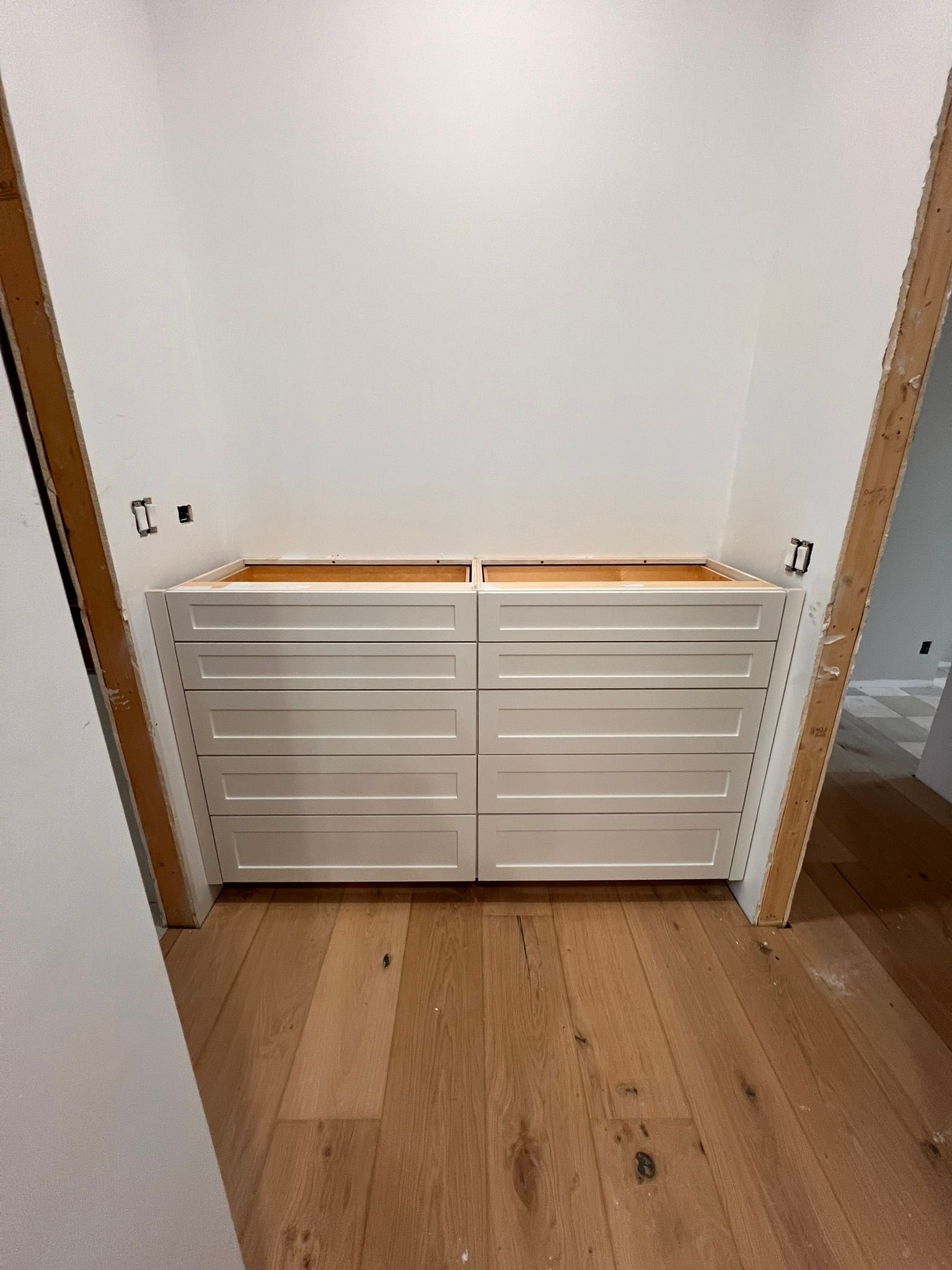 White drawer cabinets in a recessed space, wood floor, light-colored walls.