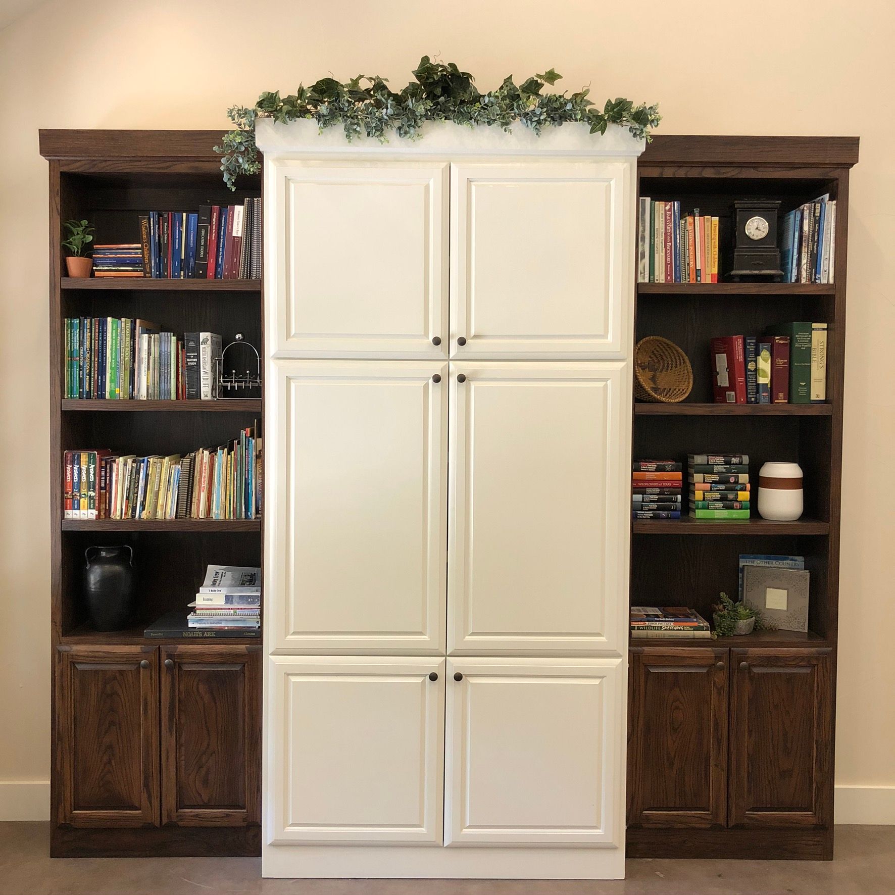 Built-in bookshelves flank a white cabinet. Books and decor fill the shelves. Greenery tops the cabinet.