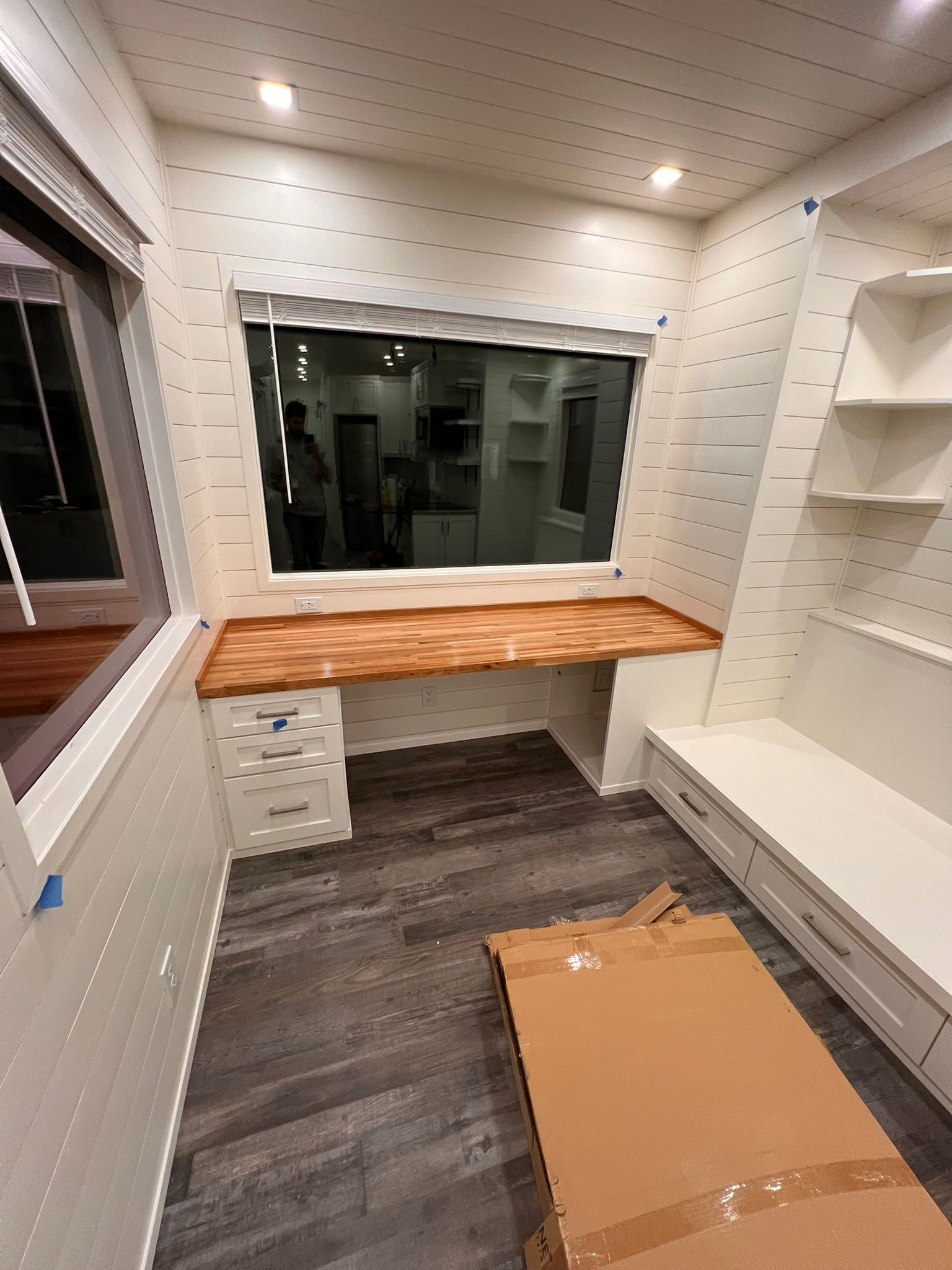 Interior with desk under window, built-in shelving and seating. Cardboard box on floor.