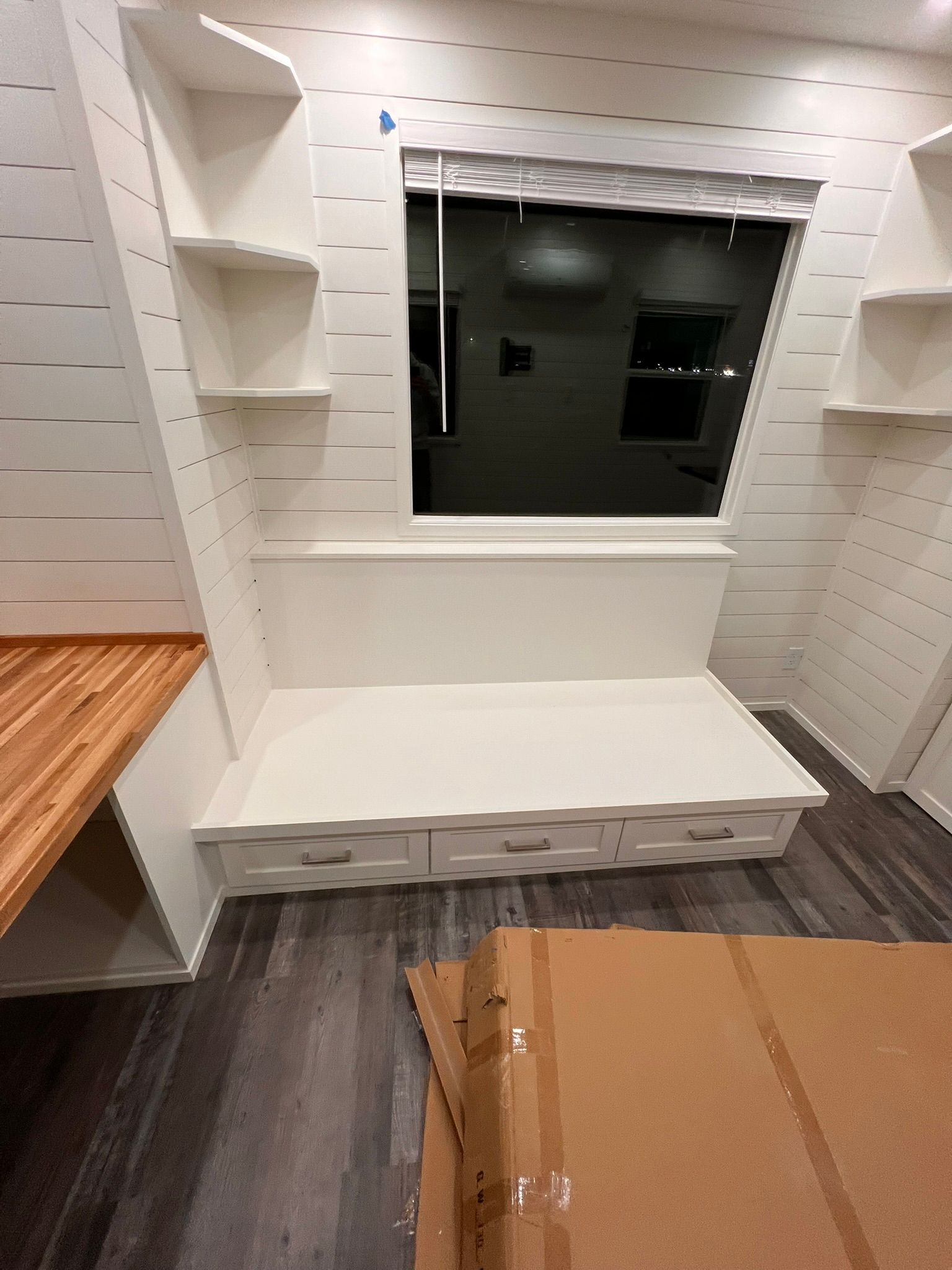 Interior with built-in bench seating, drawers, and shelving, next to a window with a shade, in a modern, white-walled space.