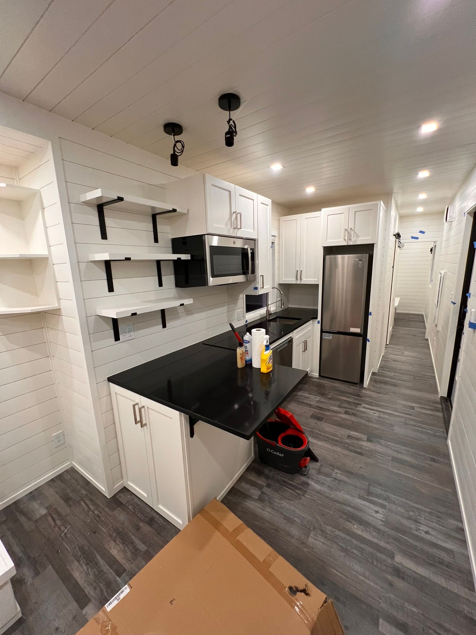 Modern kitchen with white cabinets, black countertop, stainless steel appliances, and gray flooring.
